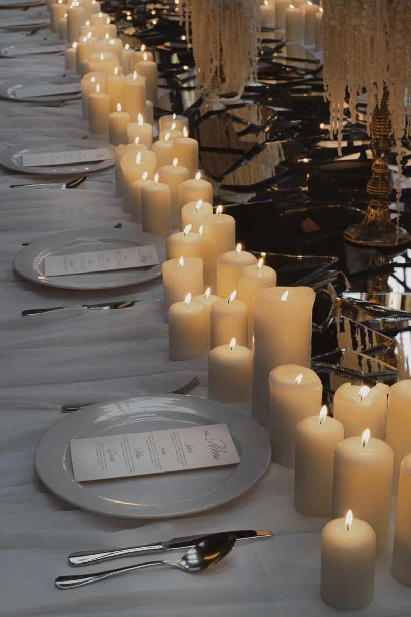 Ein festlich gedeckter Tisch mit vielen weißen Kerzen und Tellern, vermutlich für eine Gala oder ein elegantes Abendessen.