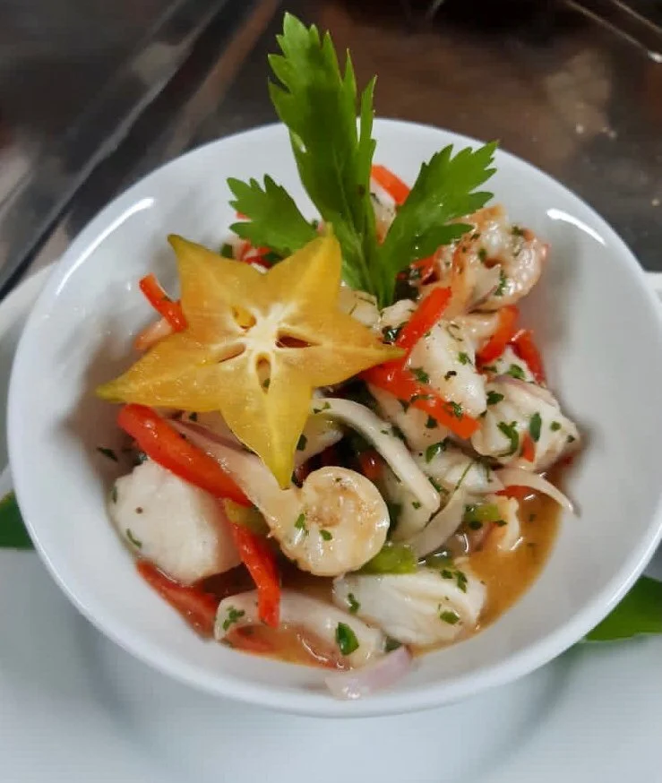 Ceviche con pimiento rojo, cilantro y una rodaja de fruta starfruit como adorno.