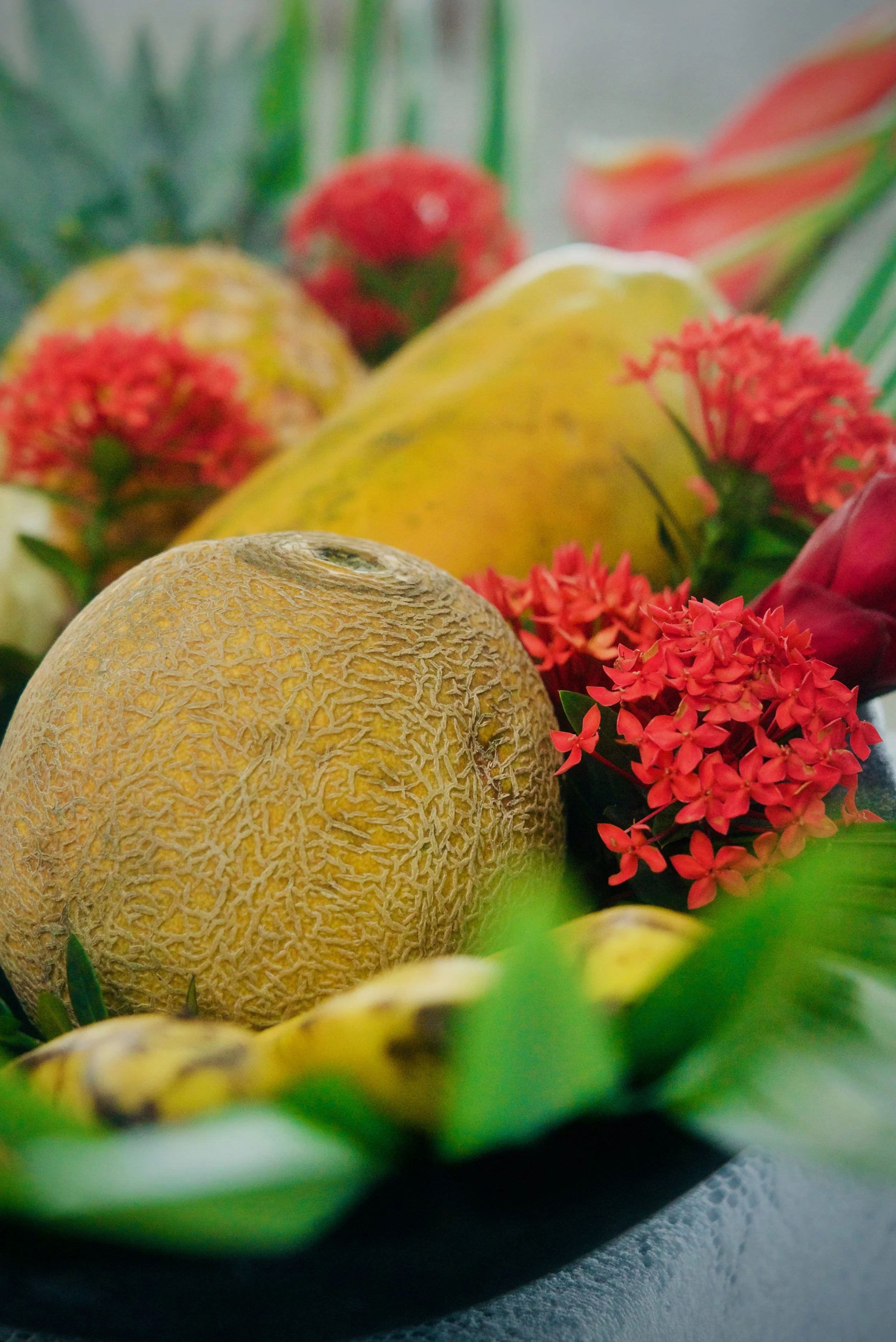 Una piña, papaya, melon y frutas tropicales y flores en un arreglo colorido.