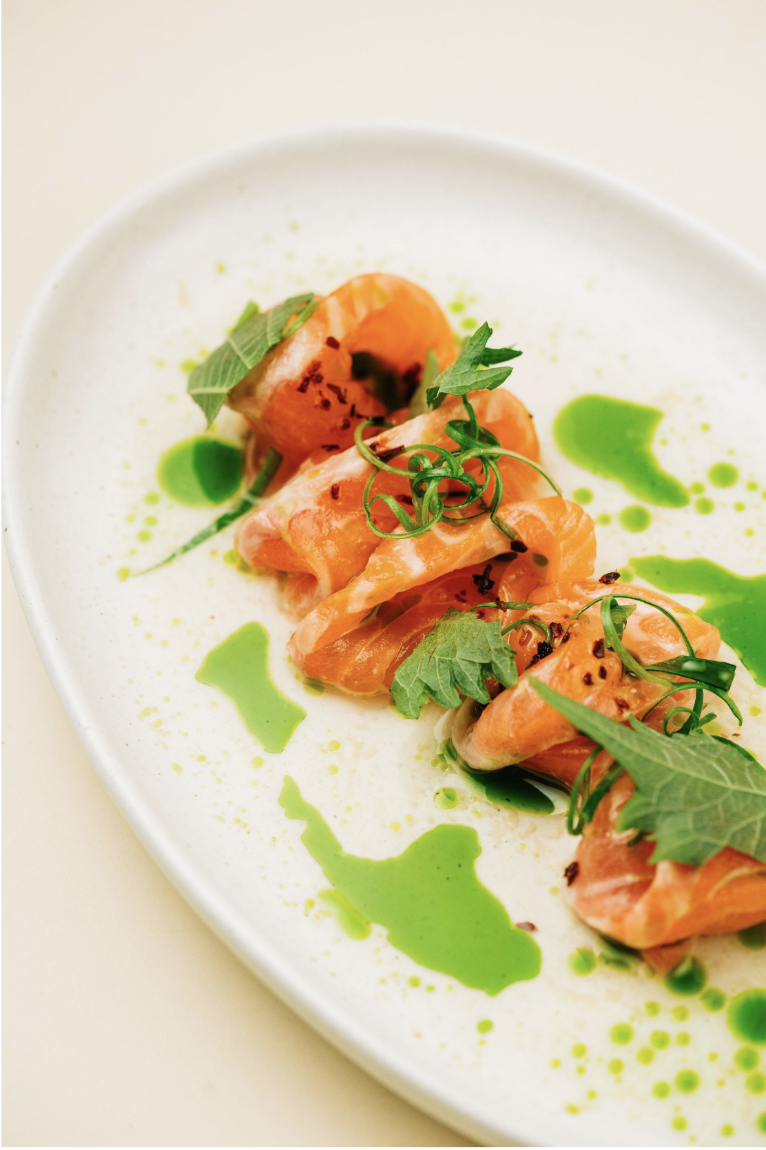 Smoked salmon garnished with fresh herbs and green sauce on a white plate.