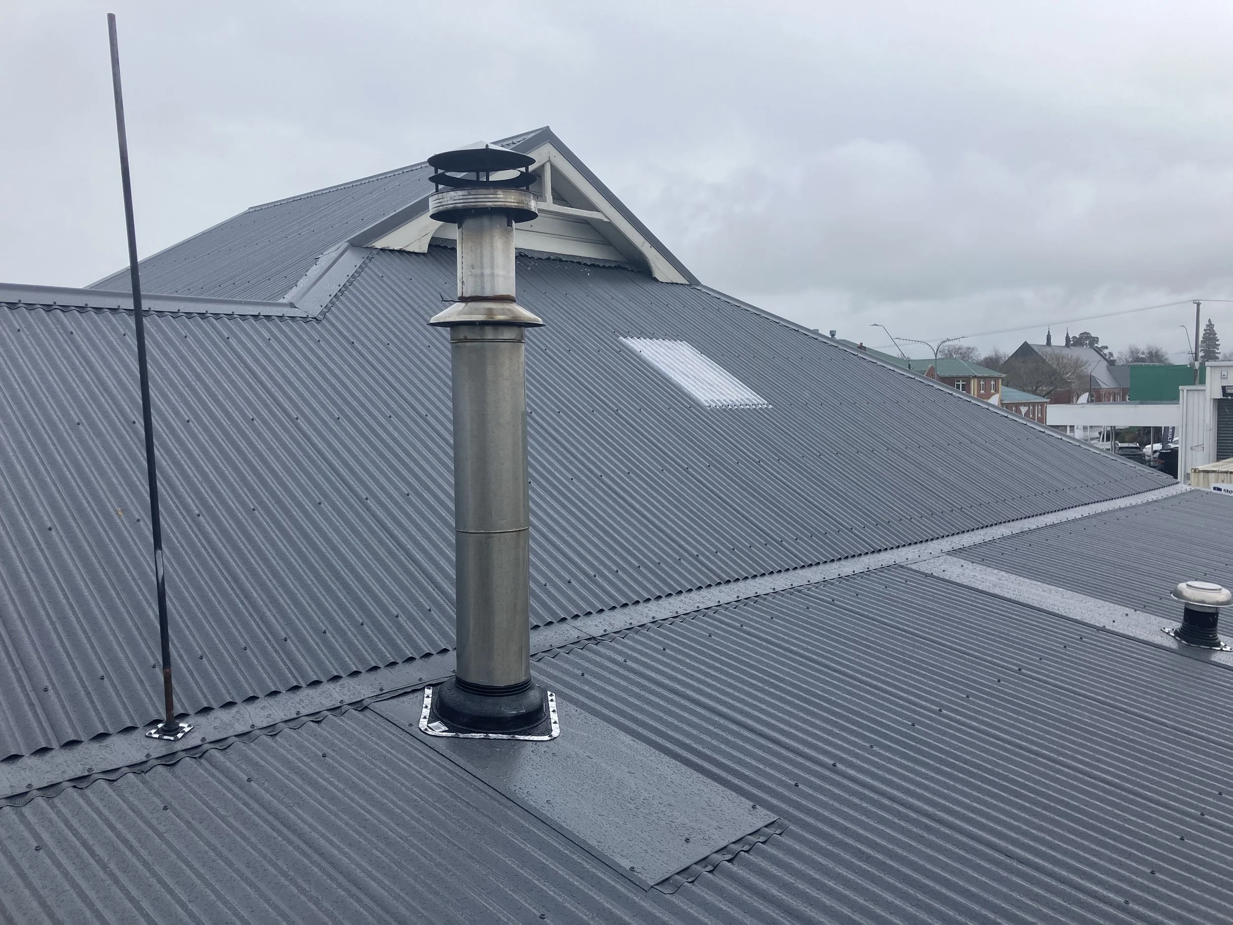 Metal roof of a building with a chimney pipe and a vent, on a cloudy day.