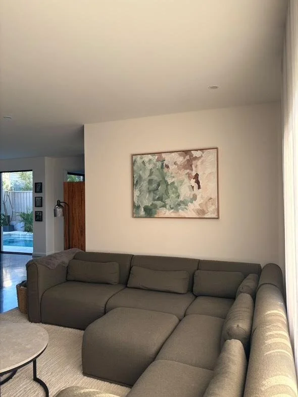 Living room with a gray sectional sofa, abstract wall art, and an open view of a patio with a pool.