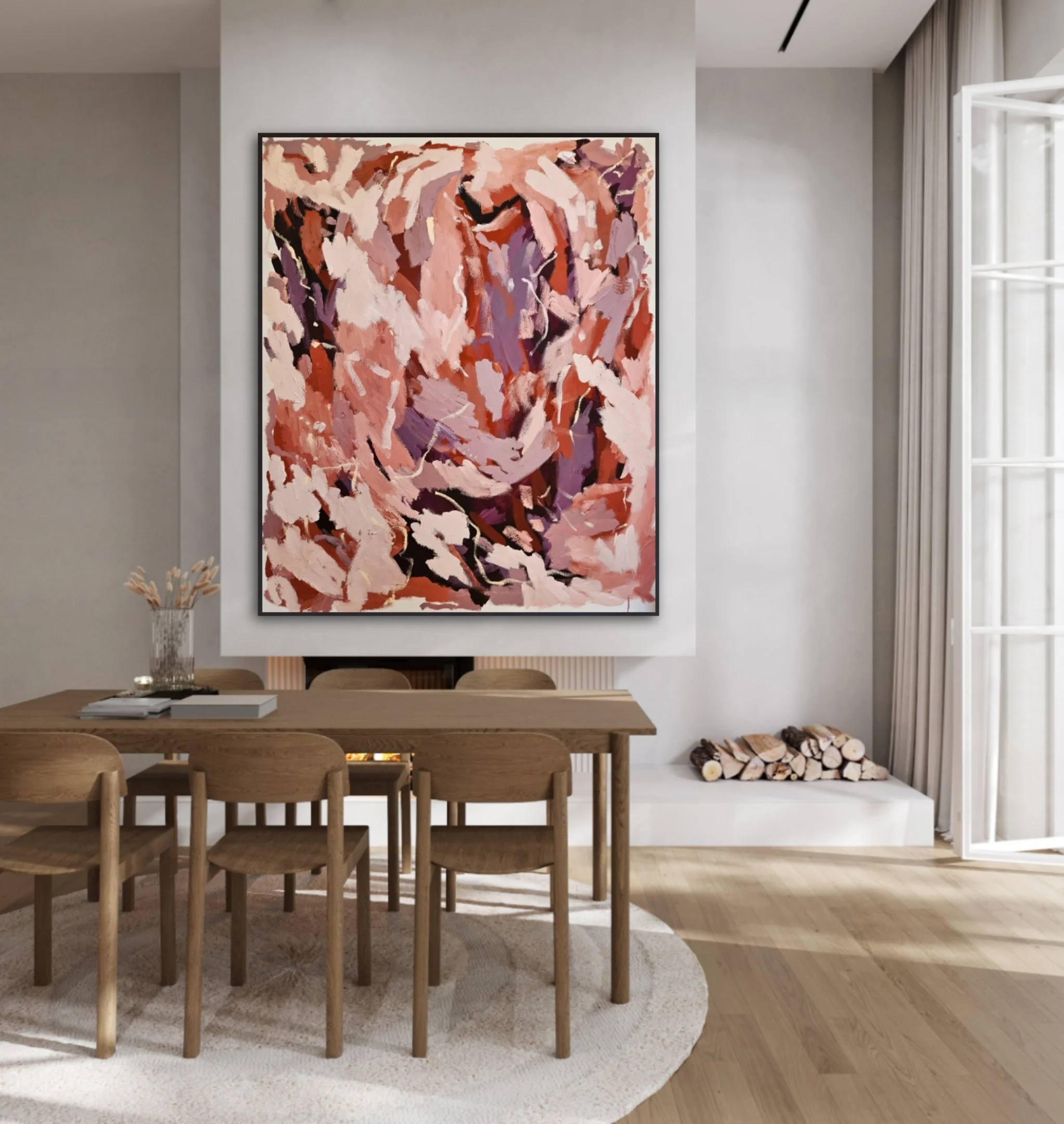 A modern dining room with a large abstract painting featuring pink, purple, and tan brushstrokes on the wall above a wooden dining table and chairs. A white fireplace with firewood stacked nearby and a window with curtains are visible.