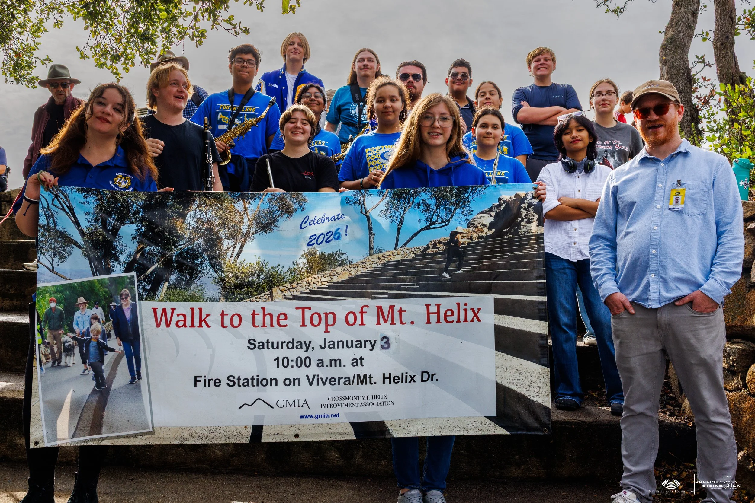 A group of people holding a banner for a walk to the top of Mt. Helix, with some standing on stairs outdoors.