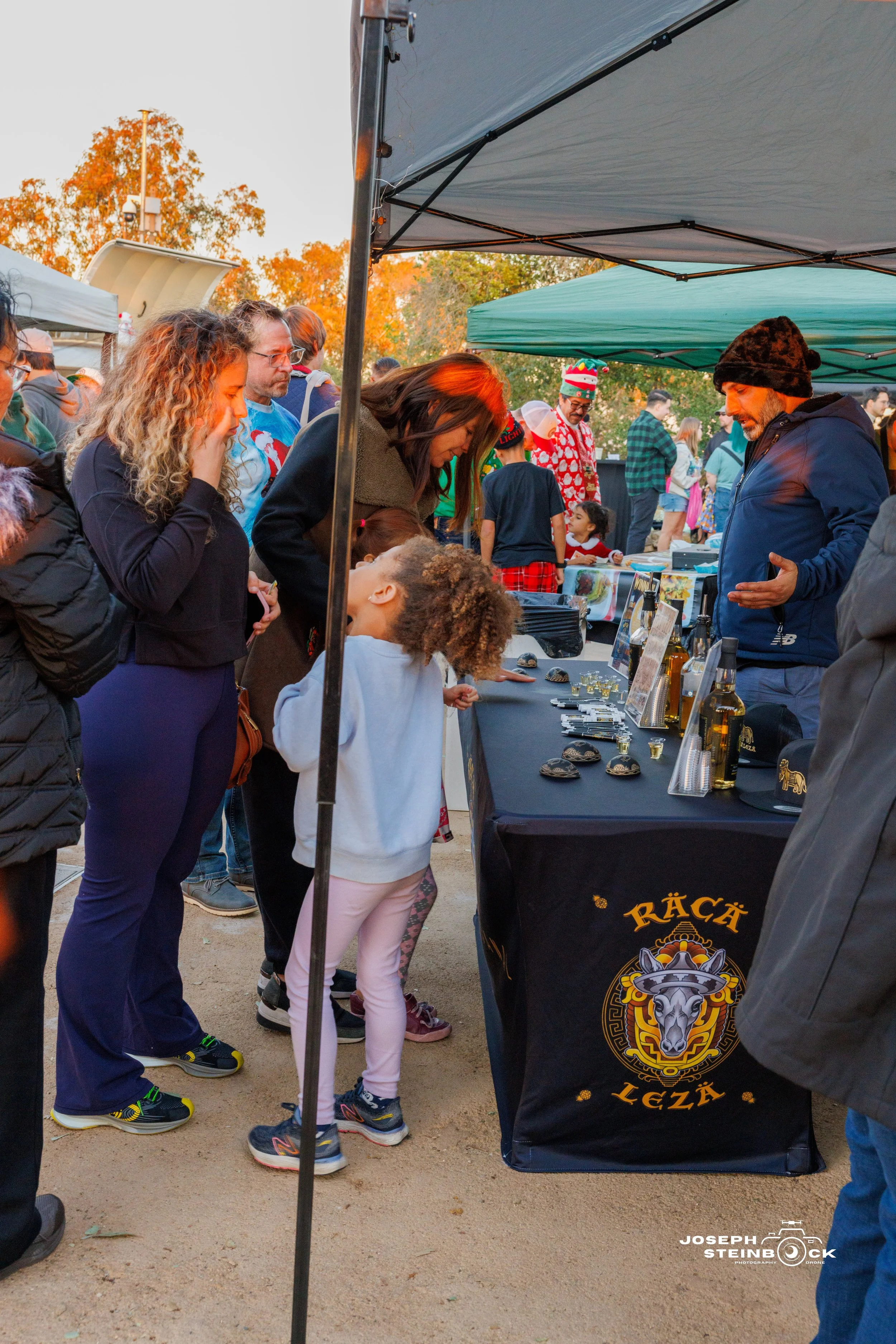 People are gathered at a vendor stall selling jewelry and accessories at an outdoor event during autumn.