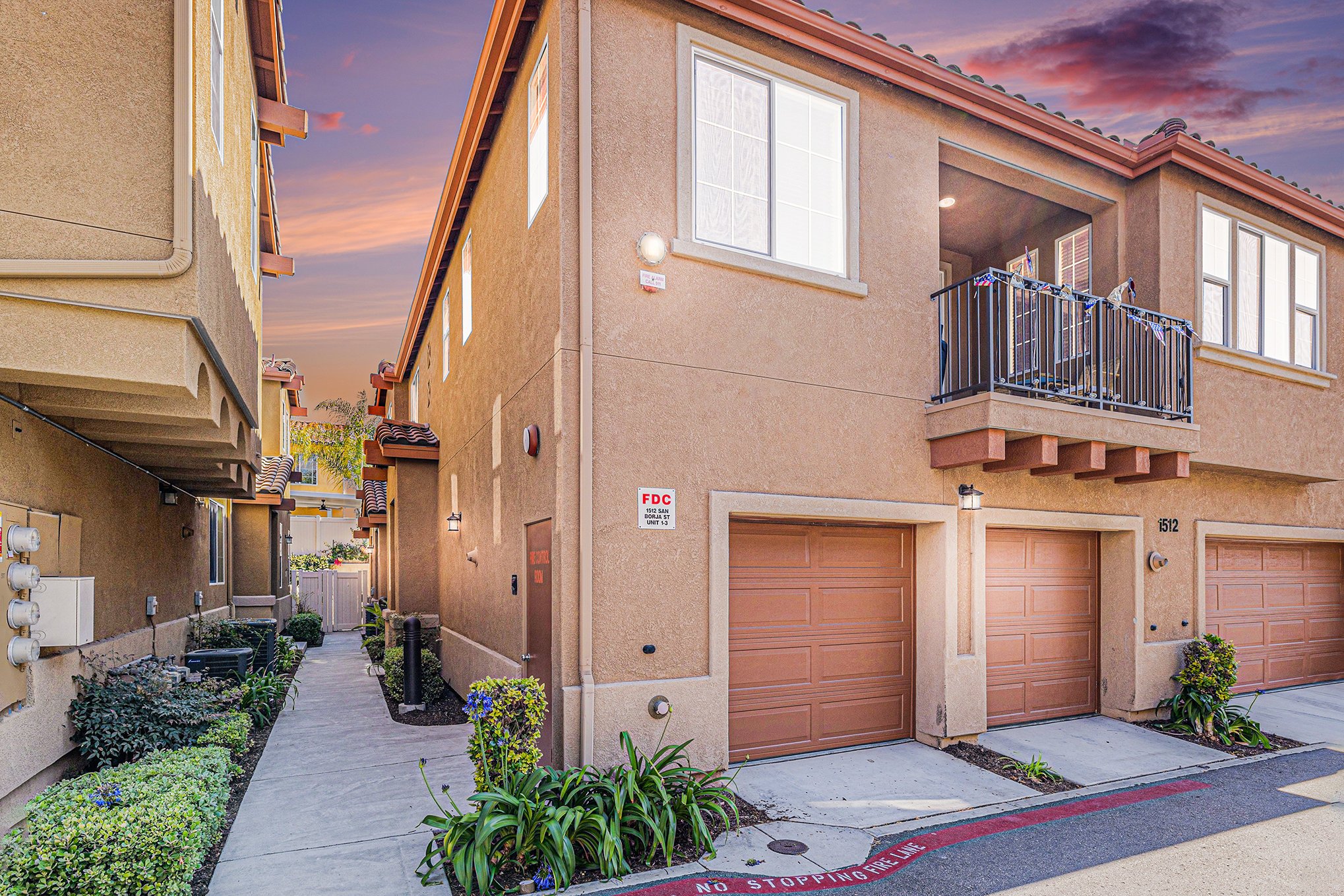 Multilevel residential apartment buildings with beige stucco exteriors, tan garage doors, and small balconies, under a sunset sky.