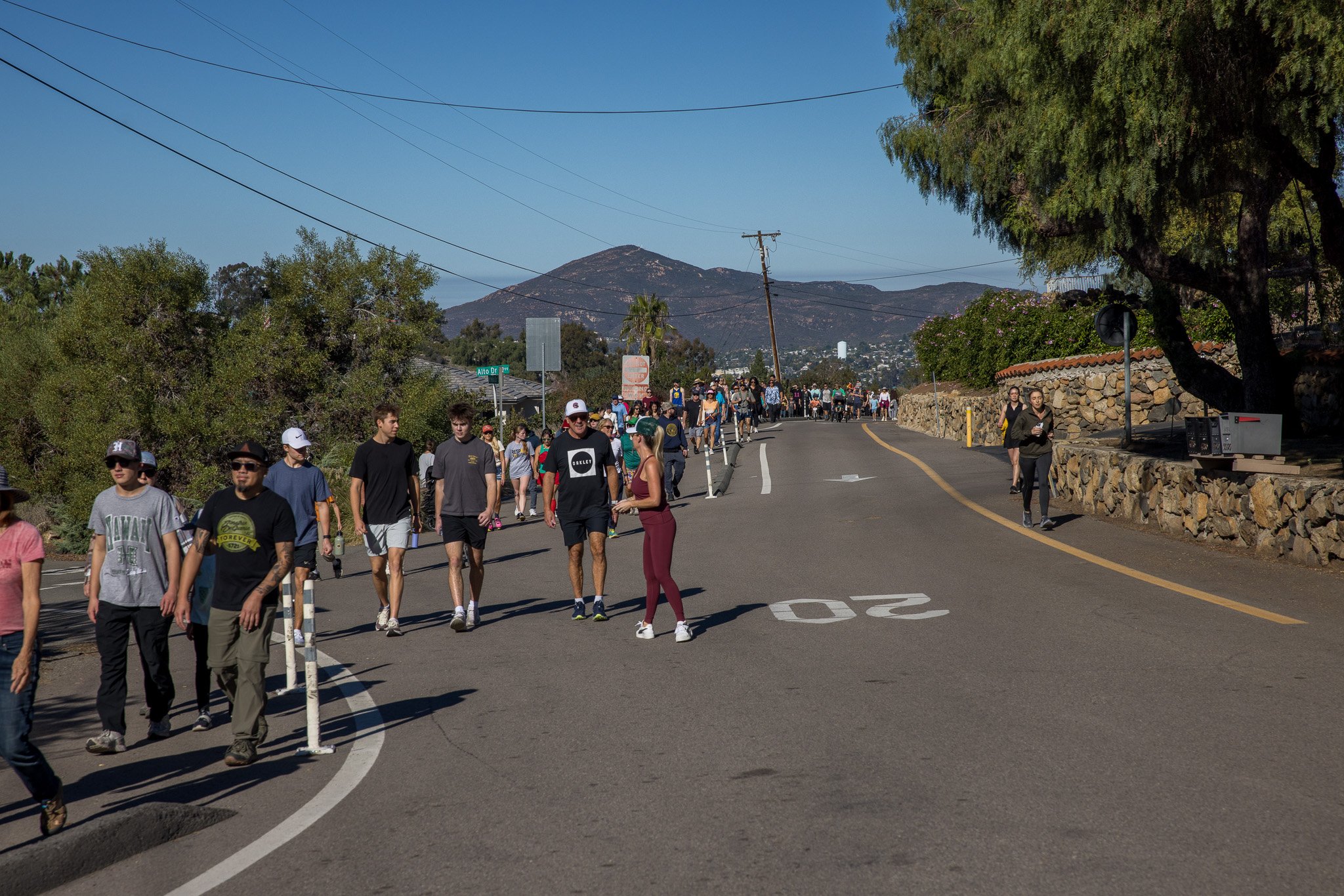 People walking on a hilly street with a mountain in the background during daytime.