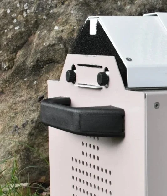 Close-up of a PinkyCrib with a black handle, and perforated metal pink surface.