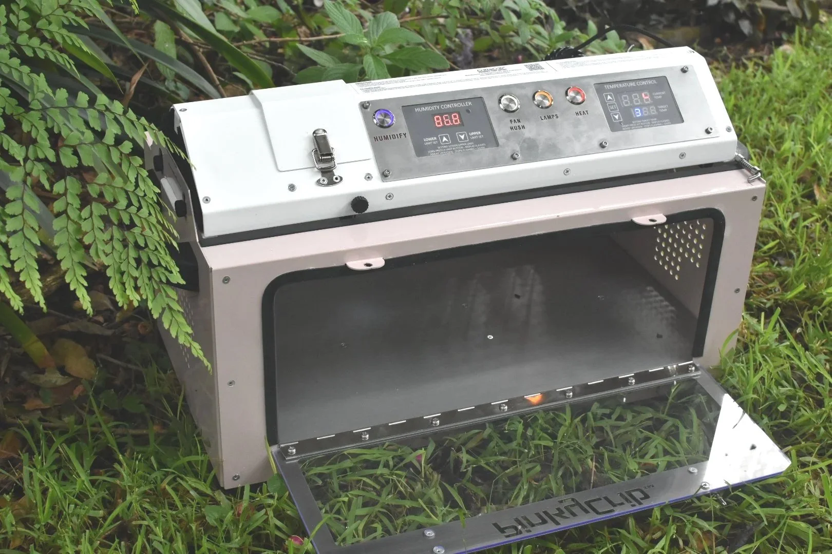 A pink and white small animal intensive care unit with a door open, placed on grass near rocks in an outdoor setting.