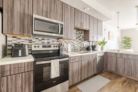 Kitchen with wood cabinets, stainless steel microwave, oven, toaster, and coffee maker, with a window and plants in the background.