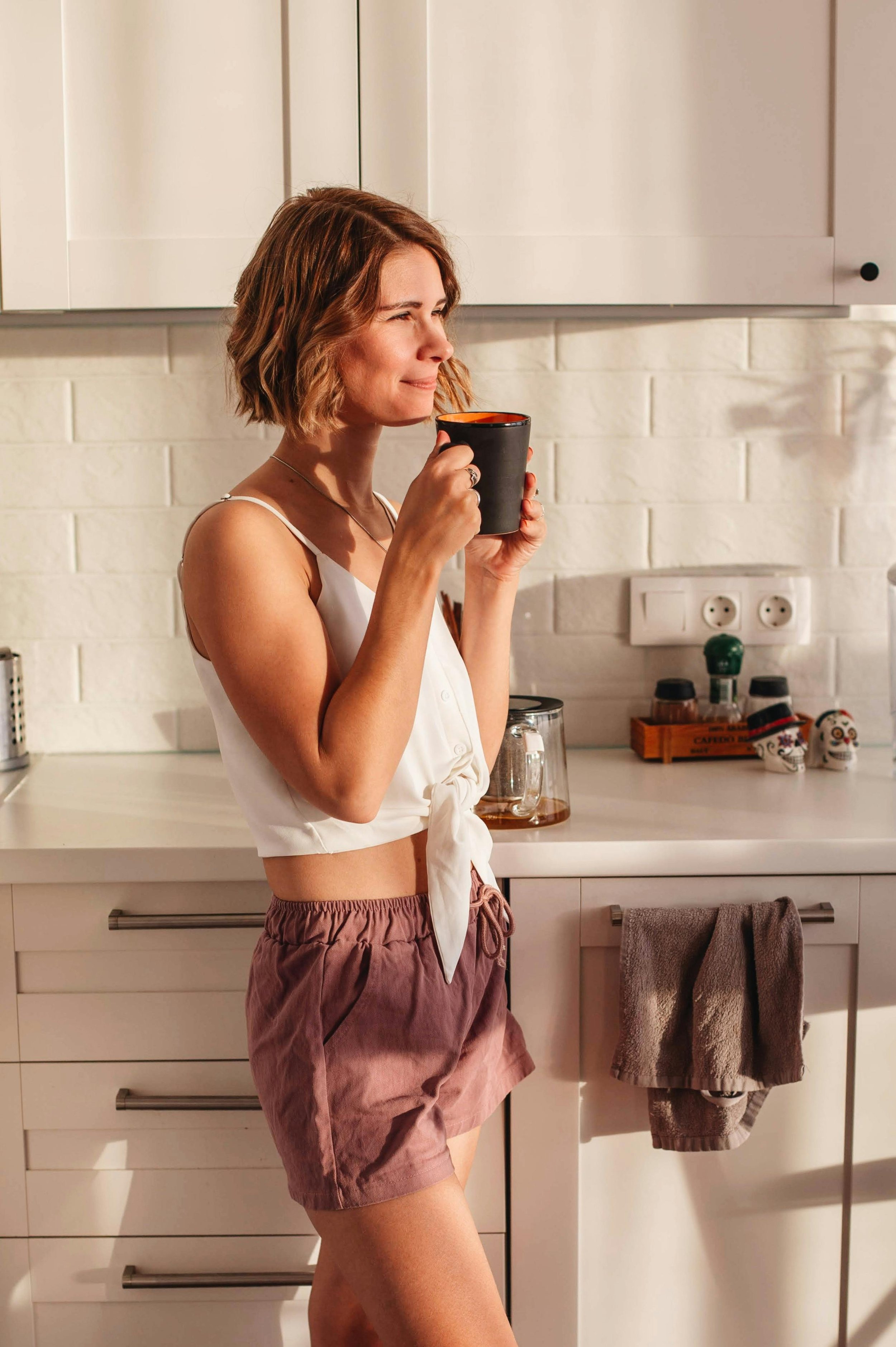 Woman standing in her kitchen holding a mug and smiling.