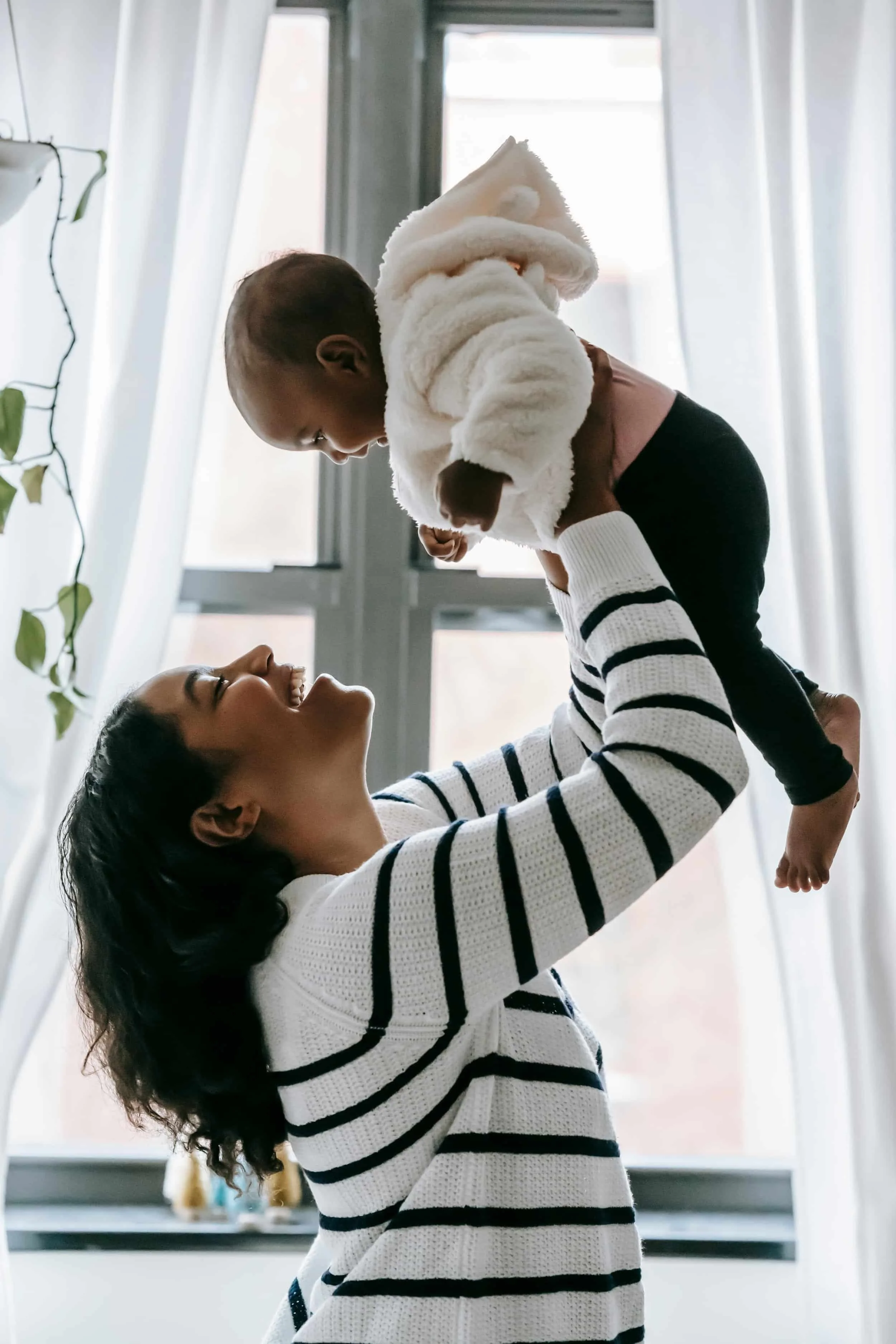 Postpartum mother holding her baby in the air while both smile at each other.