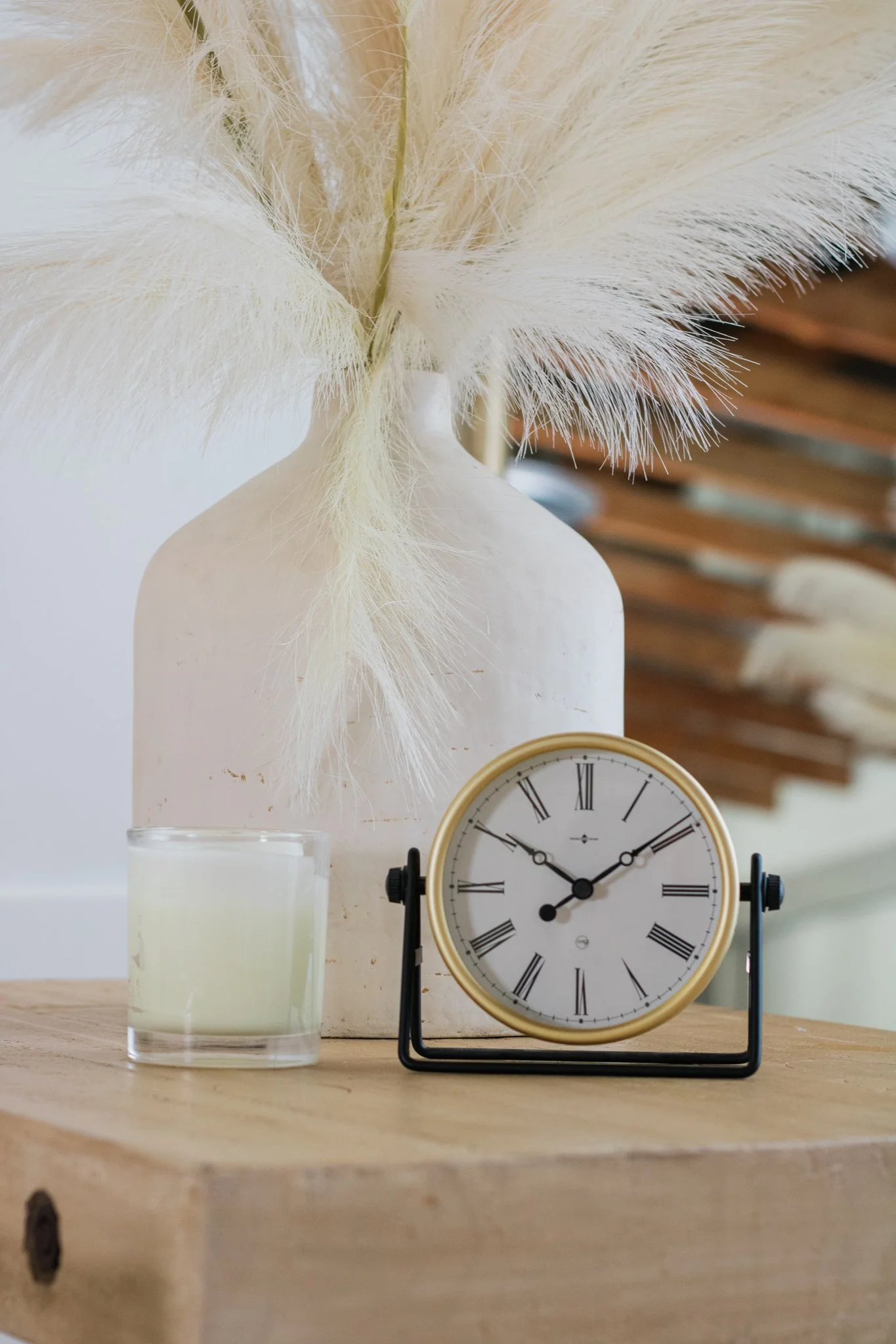 A clock sitting next to a candle in front of a decorative vase.