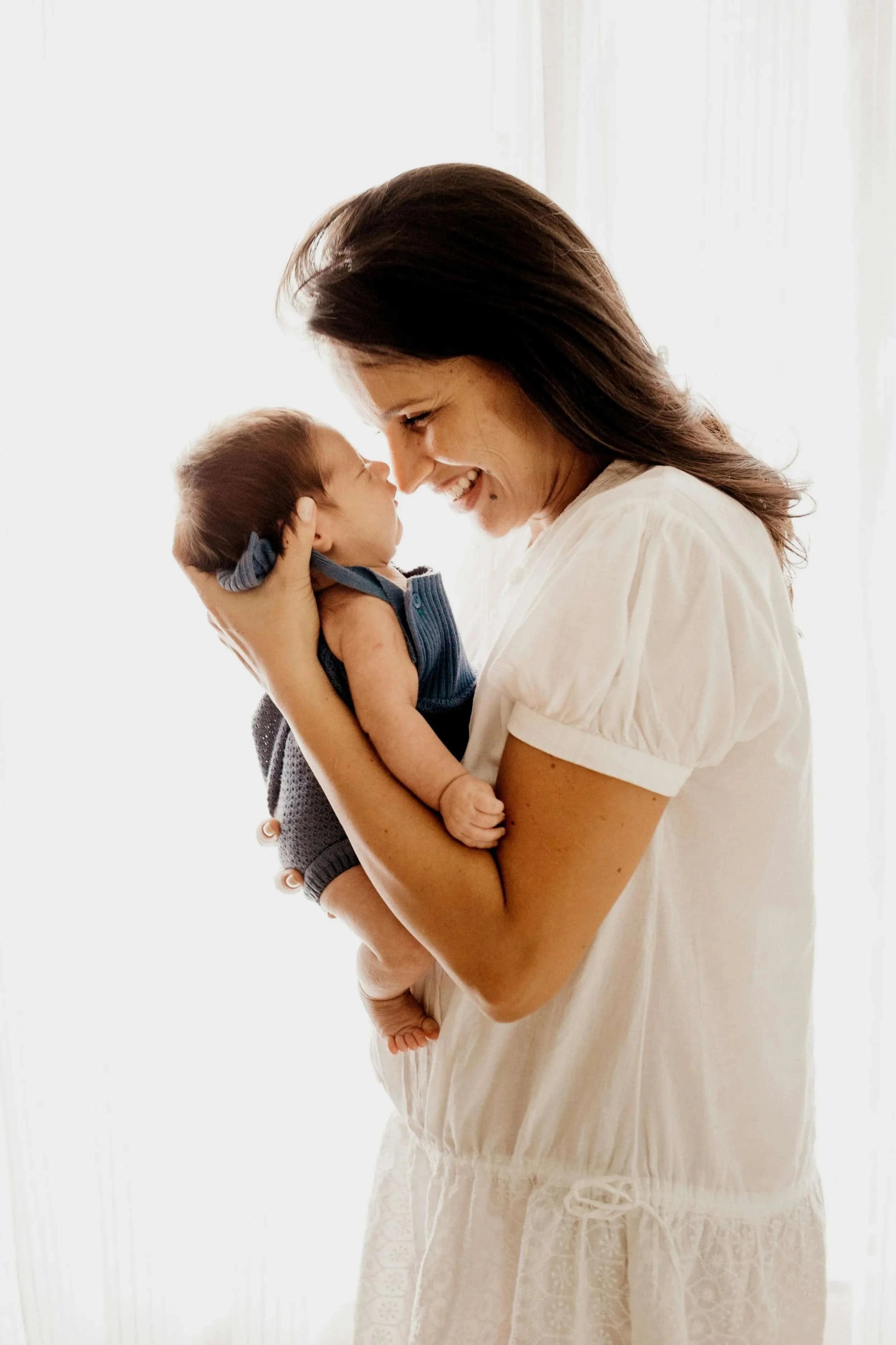 A postpartum mom smiling while holding her baby close to her face.