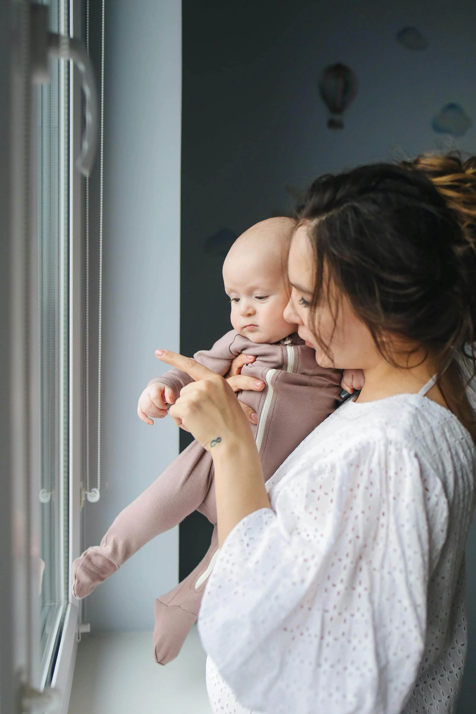 Postpartum mother holding a small baby looking out a window.