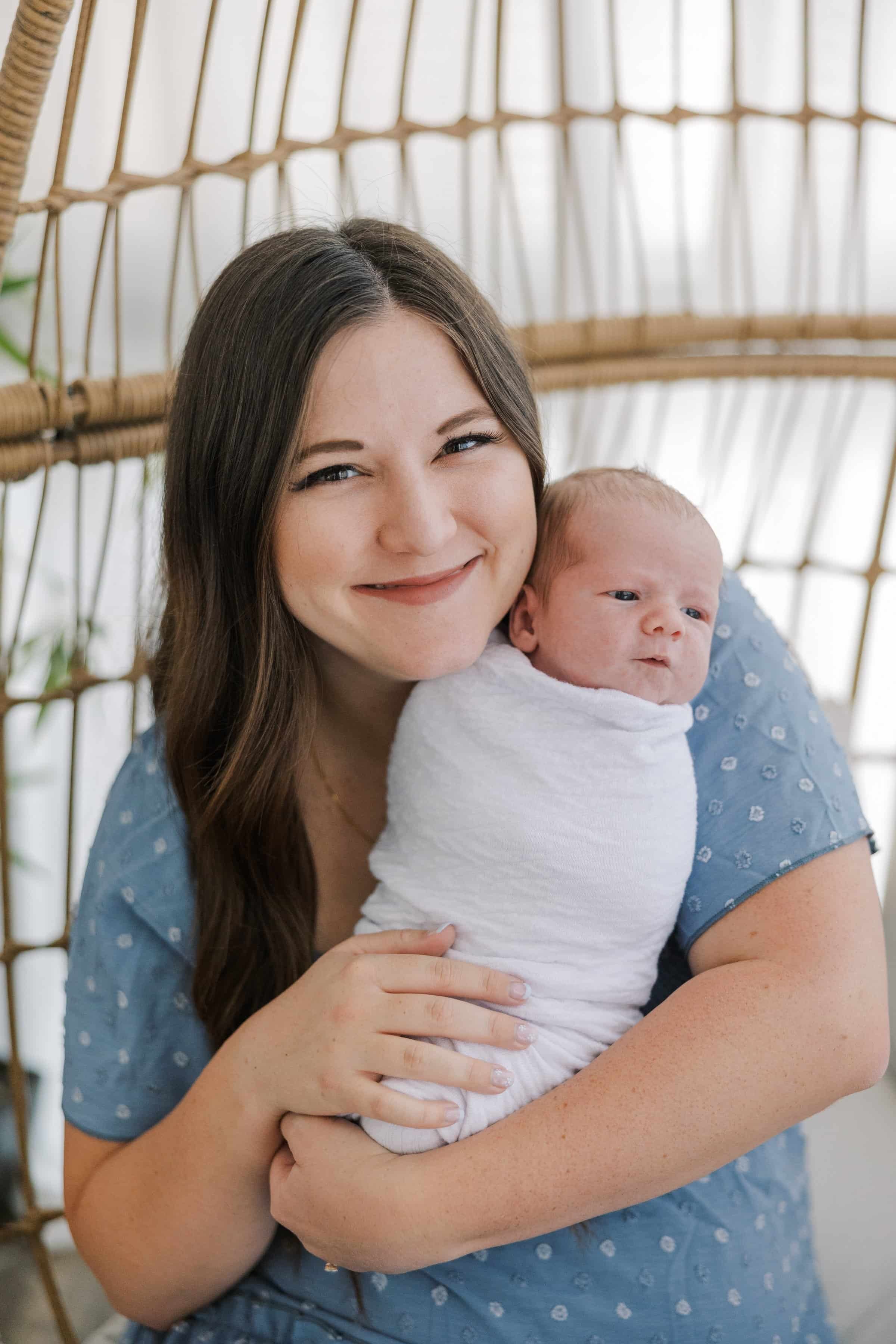 Postpartum therapist with long brown hair in a blue dress holding a newborn baby.