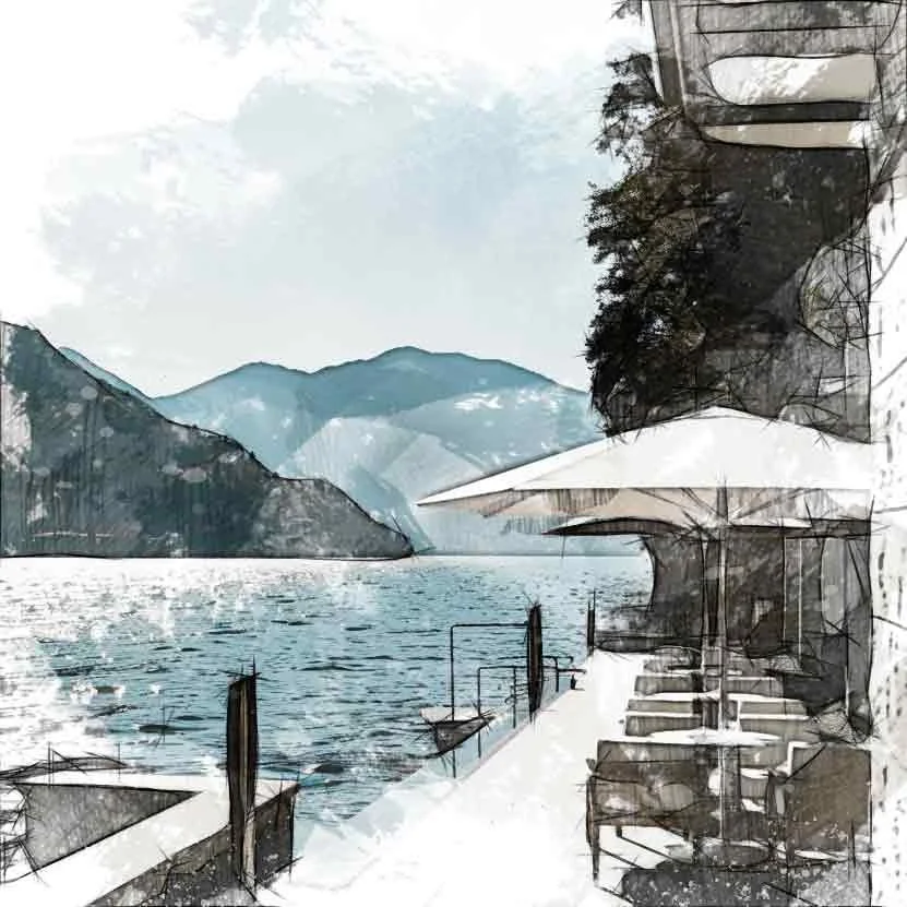 A lakeside outdoor seating area with patio tables and umbrellas next to a body of water, surrounded by mountains and trees, with partly cloudy sky.