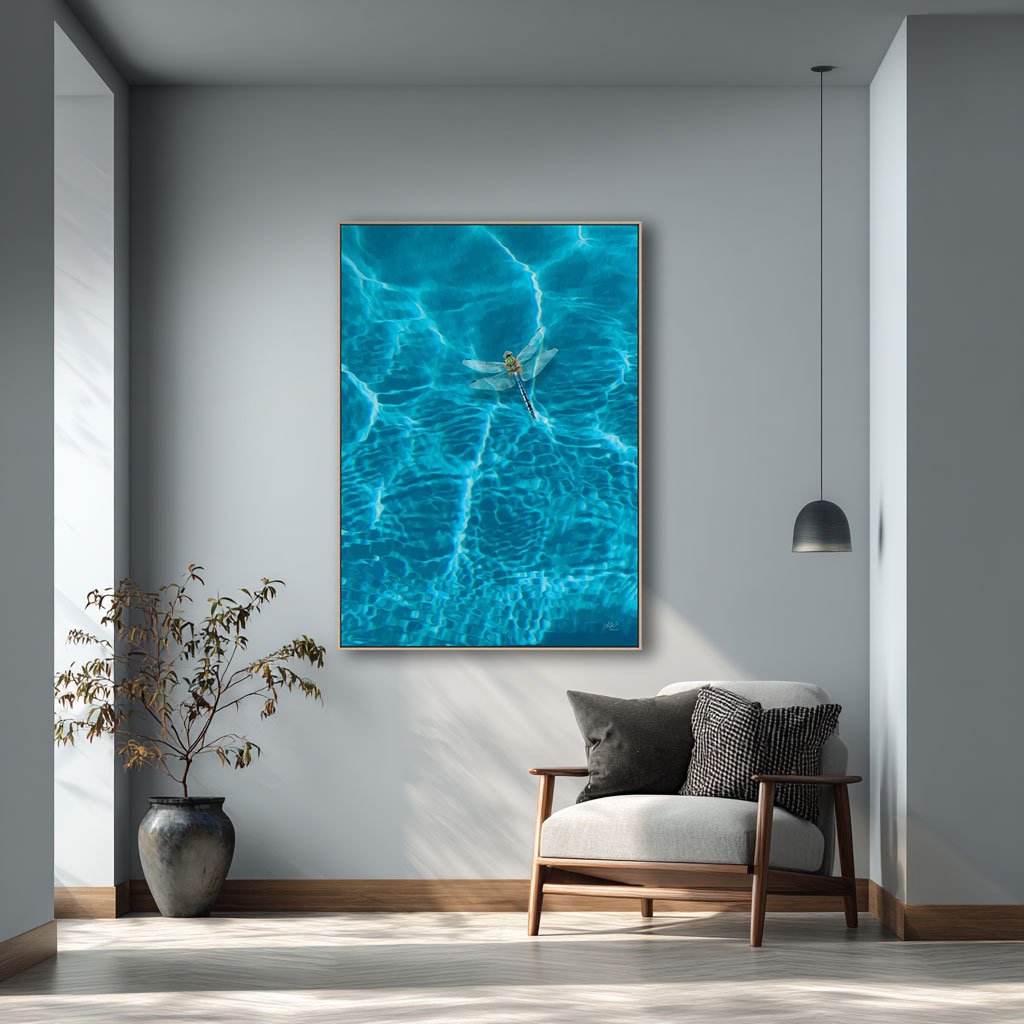 A dragonfly hovering over clear blue water. Wall art print is called Dragonfly and shown in a soft grey room.