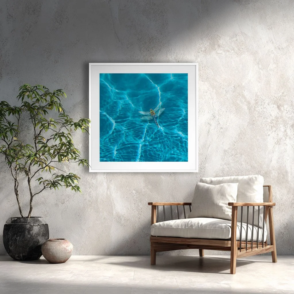 Wall are print called Dragonfly. A digital painting of a dragonfly hovering over water on a wall beside a cream chair..
