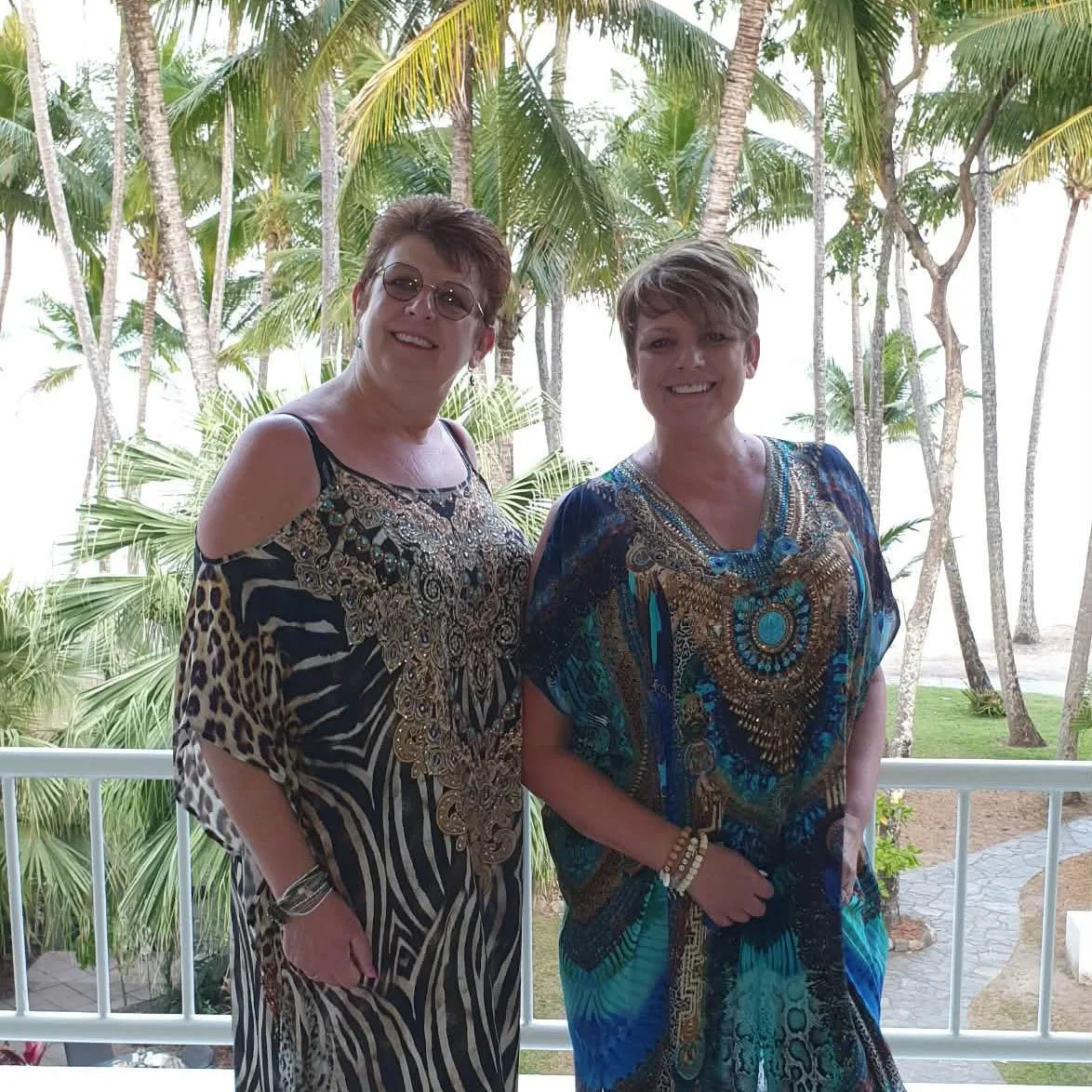 Amanda and her sister with tropical trees and waterfront in the background, smiling.