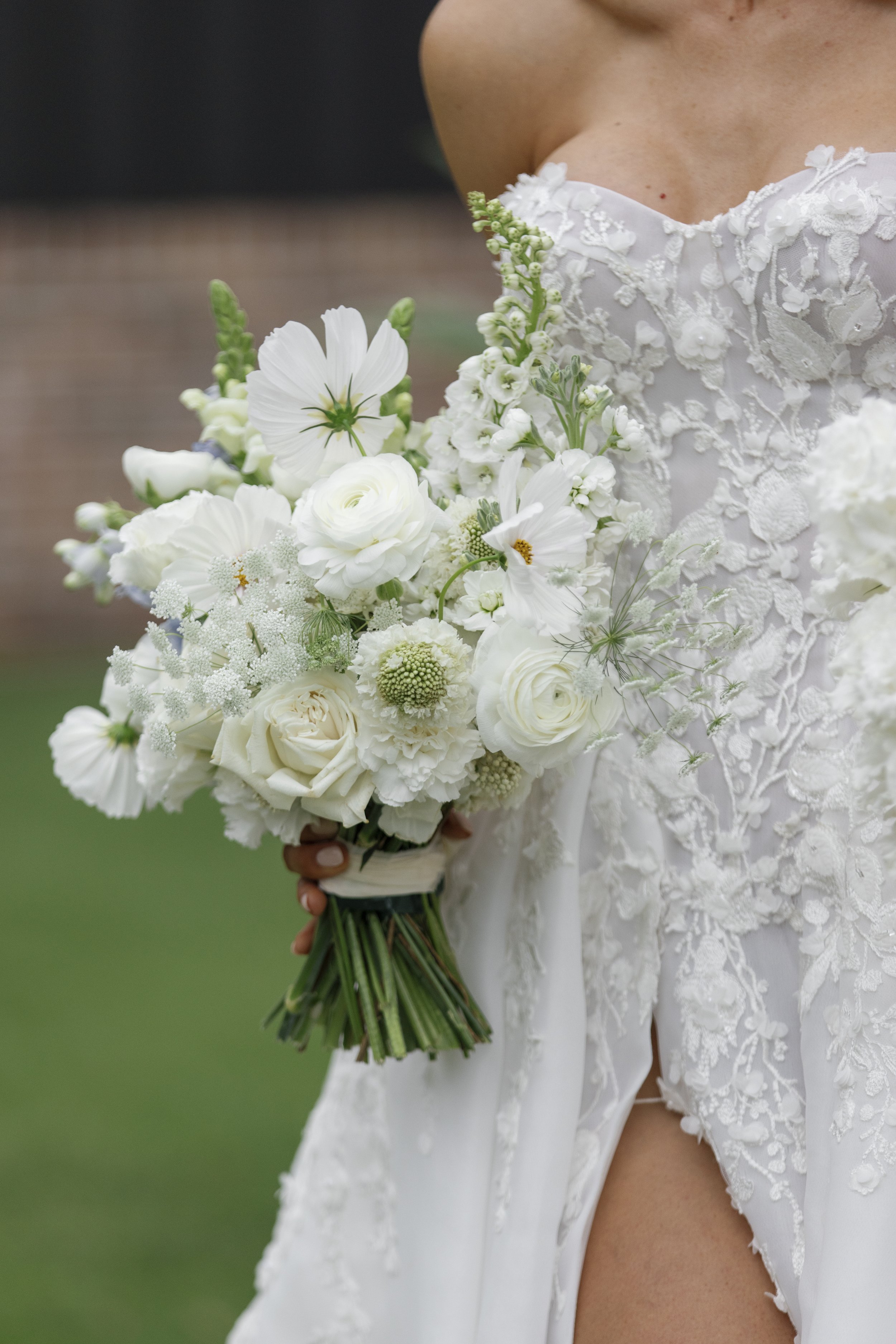 A bride holding a bouquet of white flowers, wearing a lace wedding dress.
