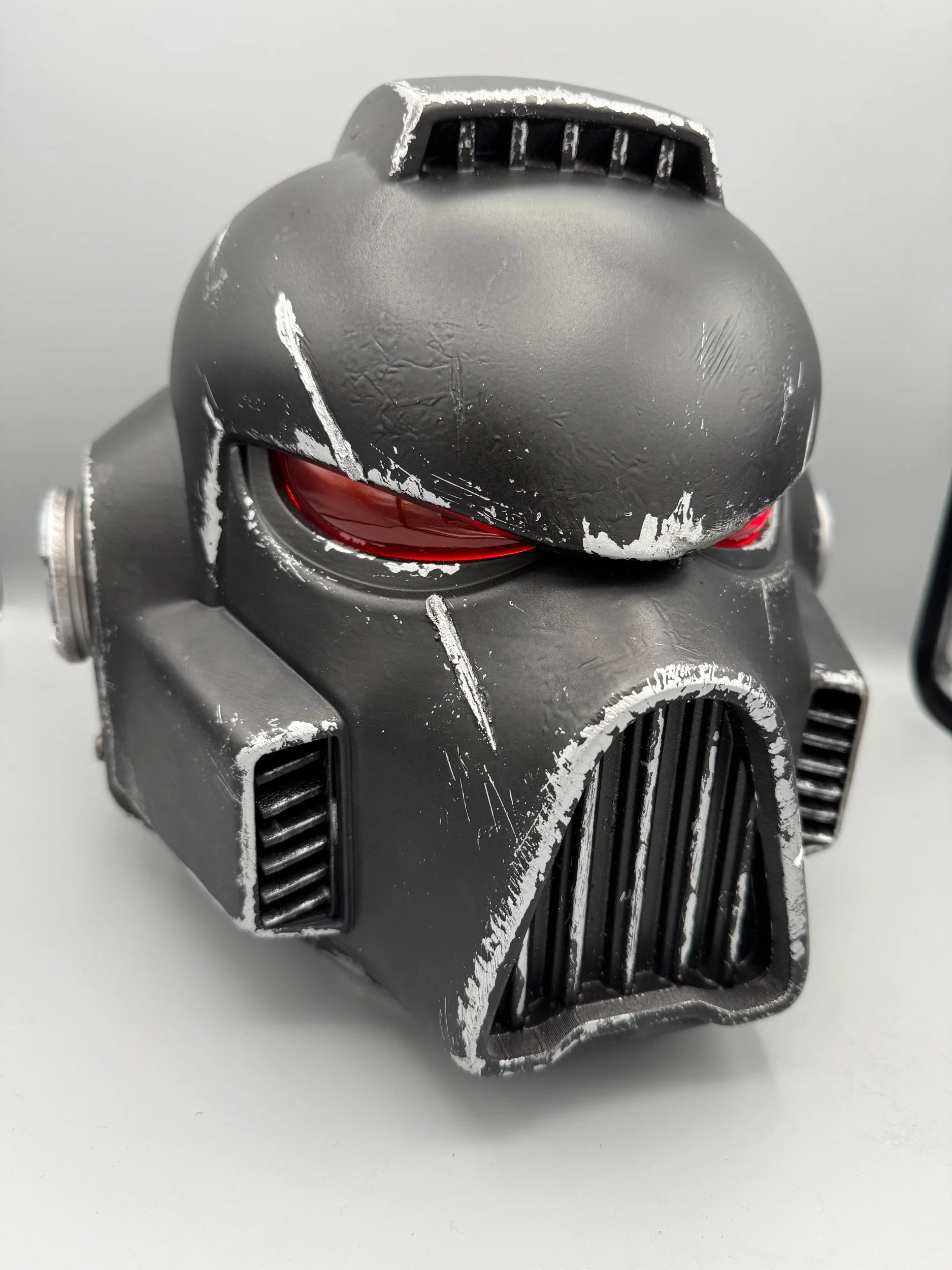 A Black Templars MK8 space marine helmet, battle-scarred look and red eyes, set against a plain background.