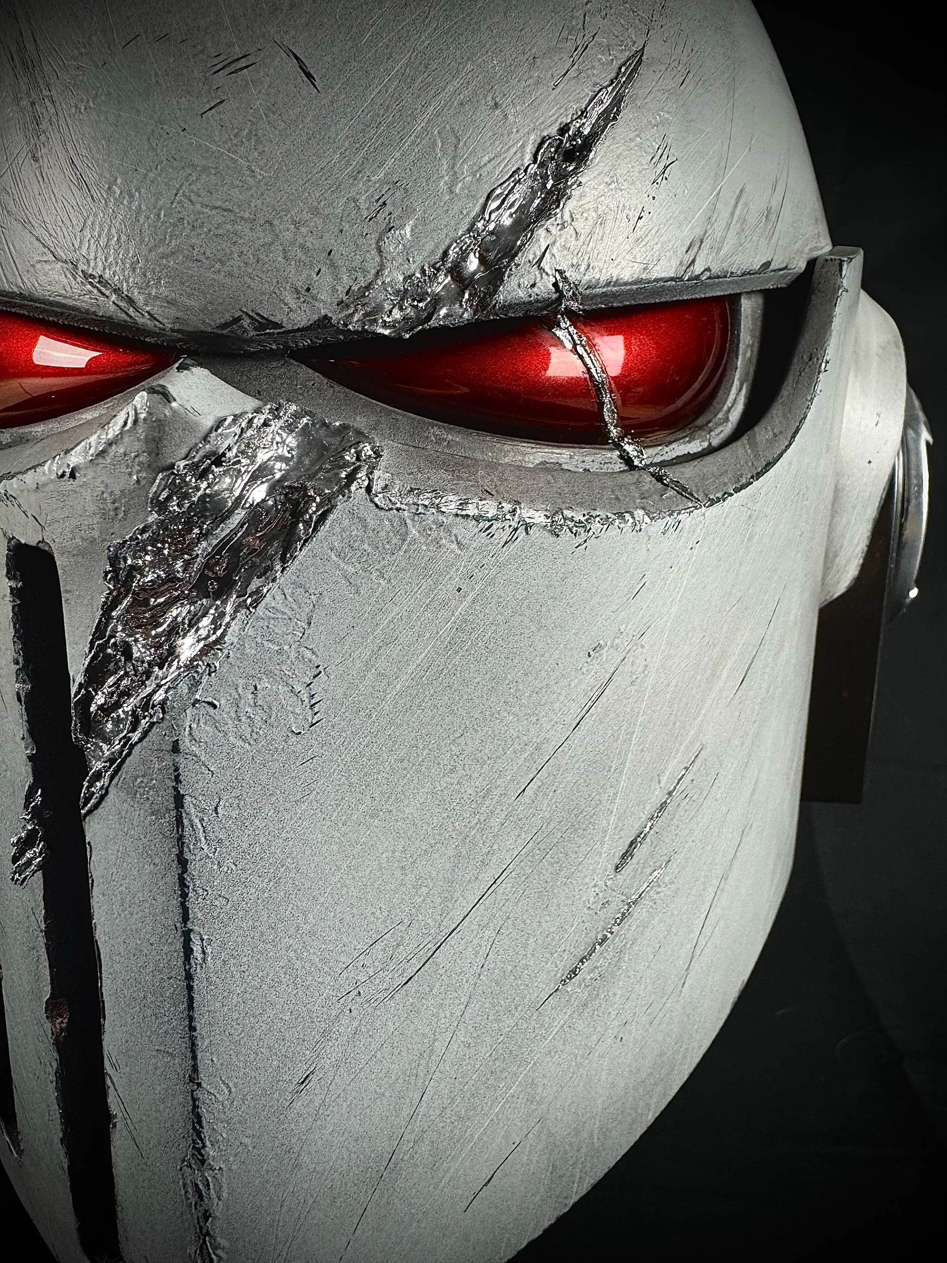 Close-up MK10 Space marine Bulwark helmet, damaged helmet with red visor, featuring scratches and a prominent crack.