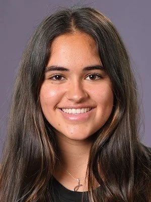 A young woman with long brown hair smiling at the camera against a plain background.