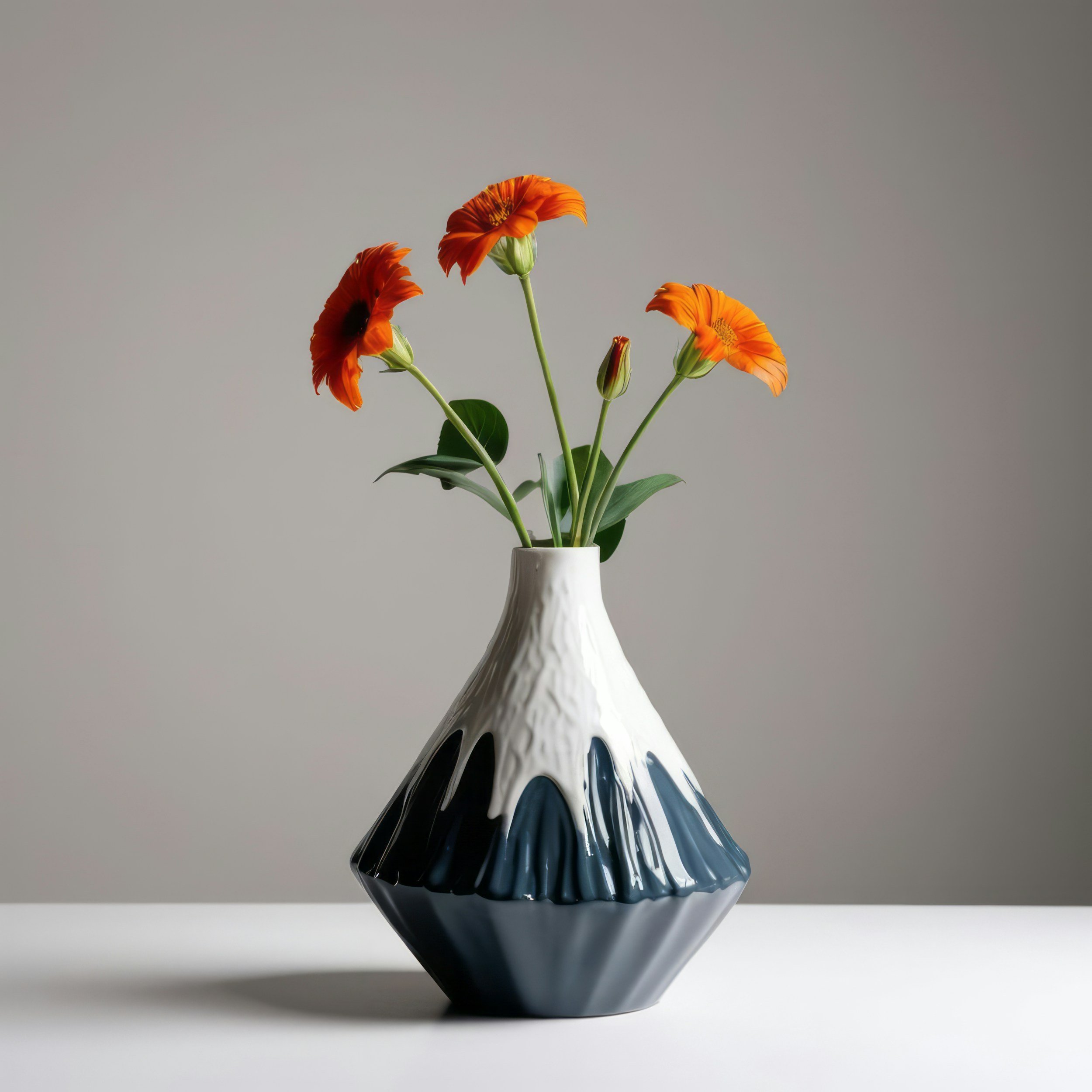 Orange flowers in a black and white ceramic vase on a white surface against a plain background.