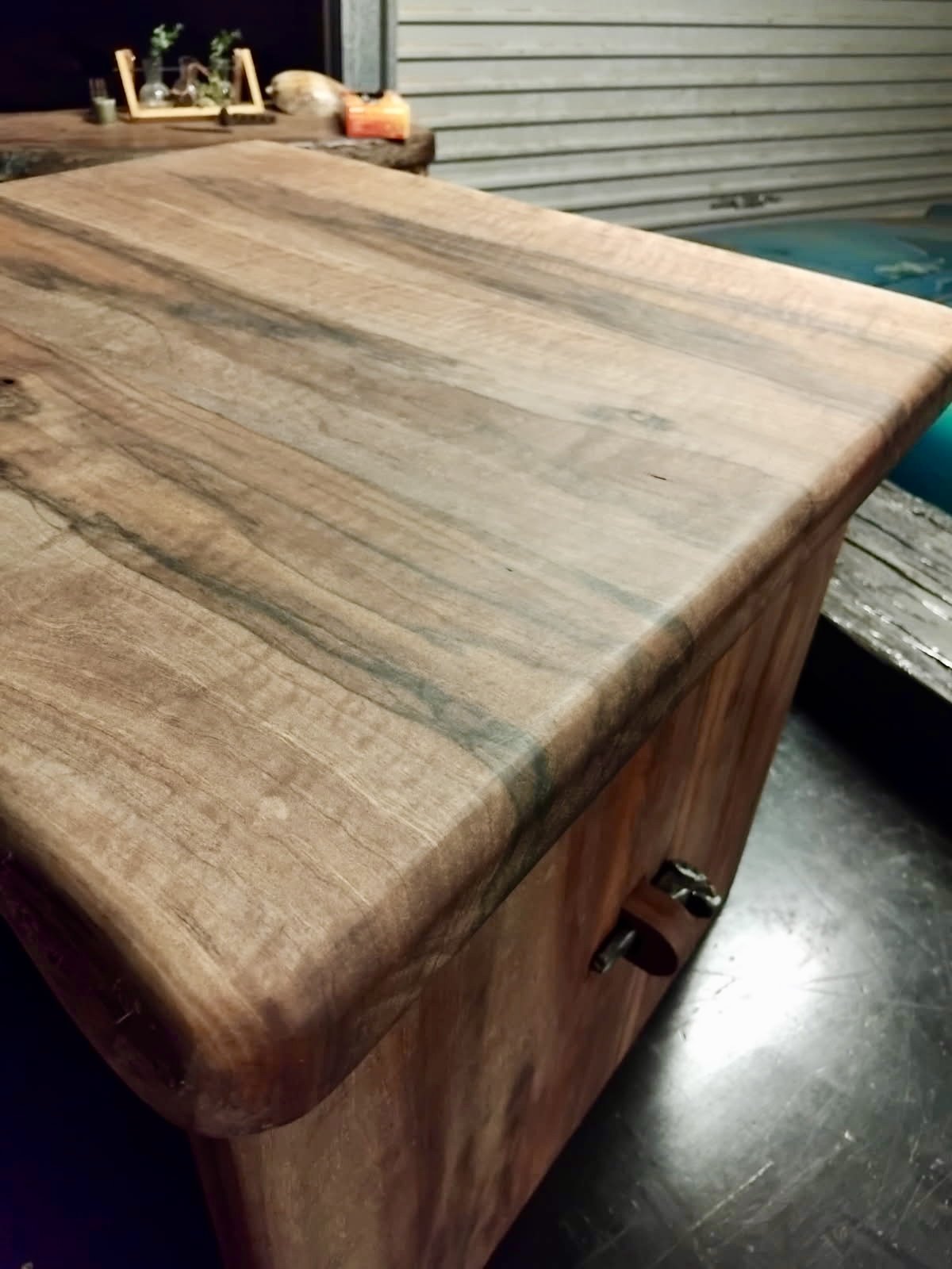 Close-up of a wooden box with rounded edges and a latch on the side, sitting on a dark surface.