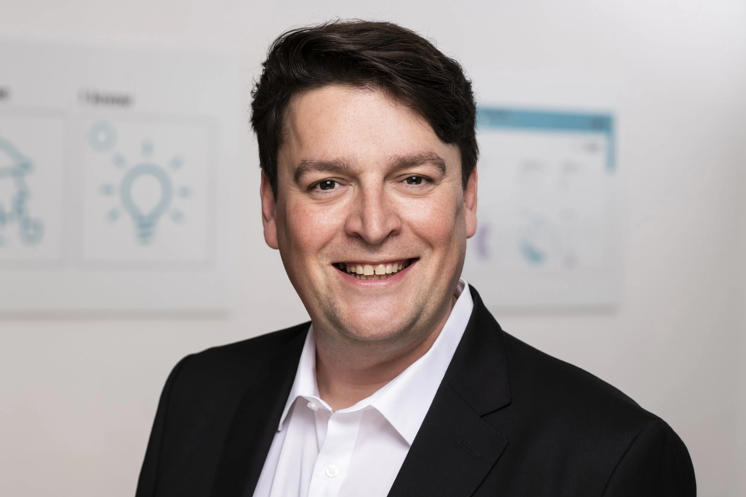 Mann in Anzug, lachend, vor Whiteboard mit Diagrammen