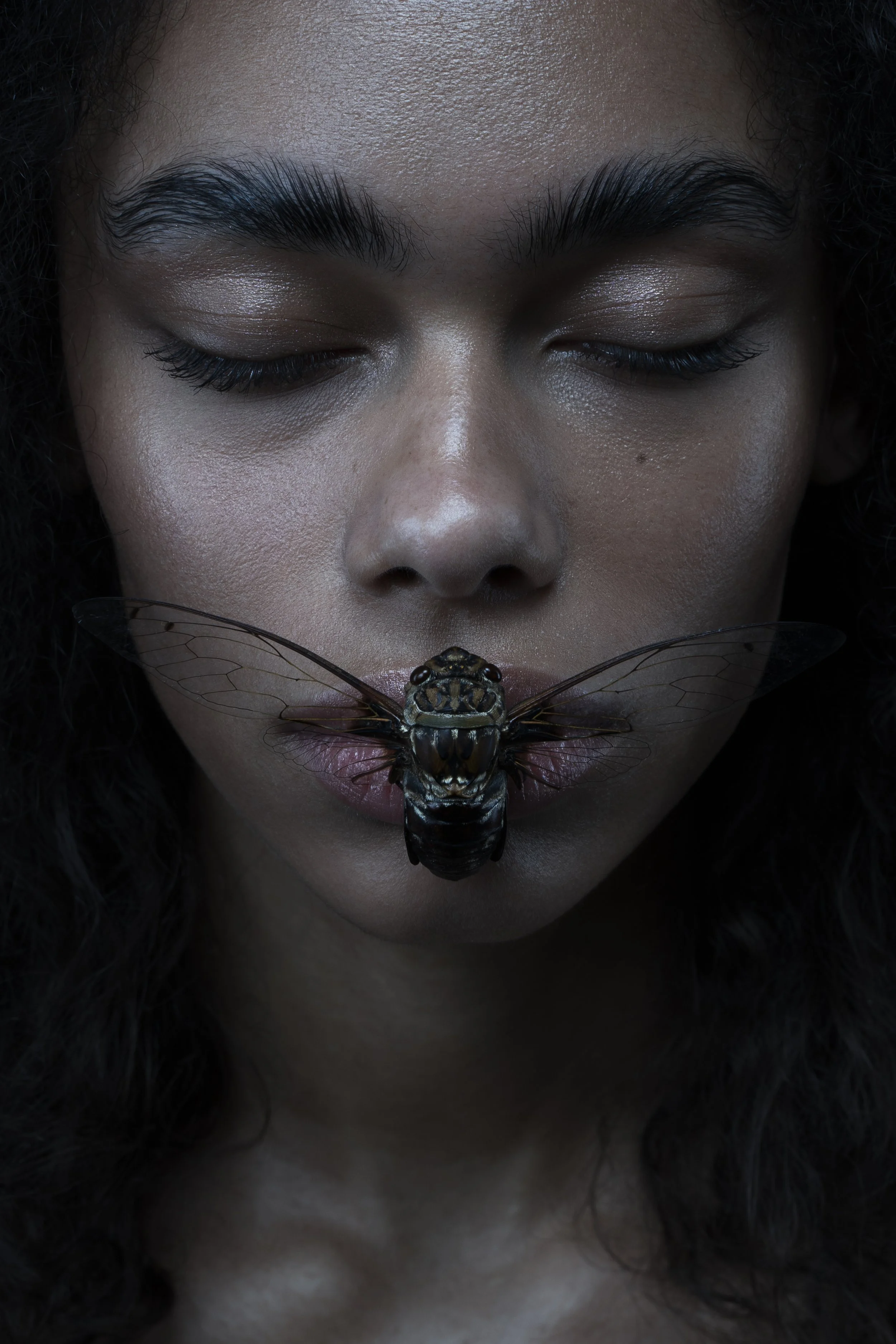 Close-up of a woman with closed eyes, holding a large insect in her mouth.