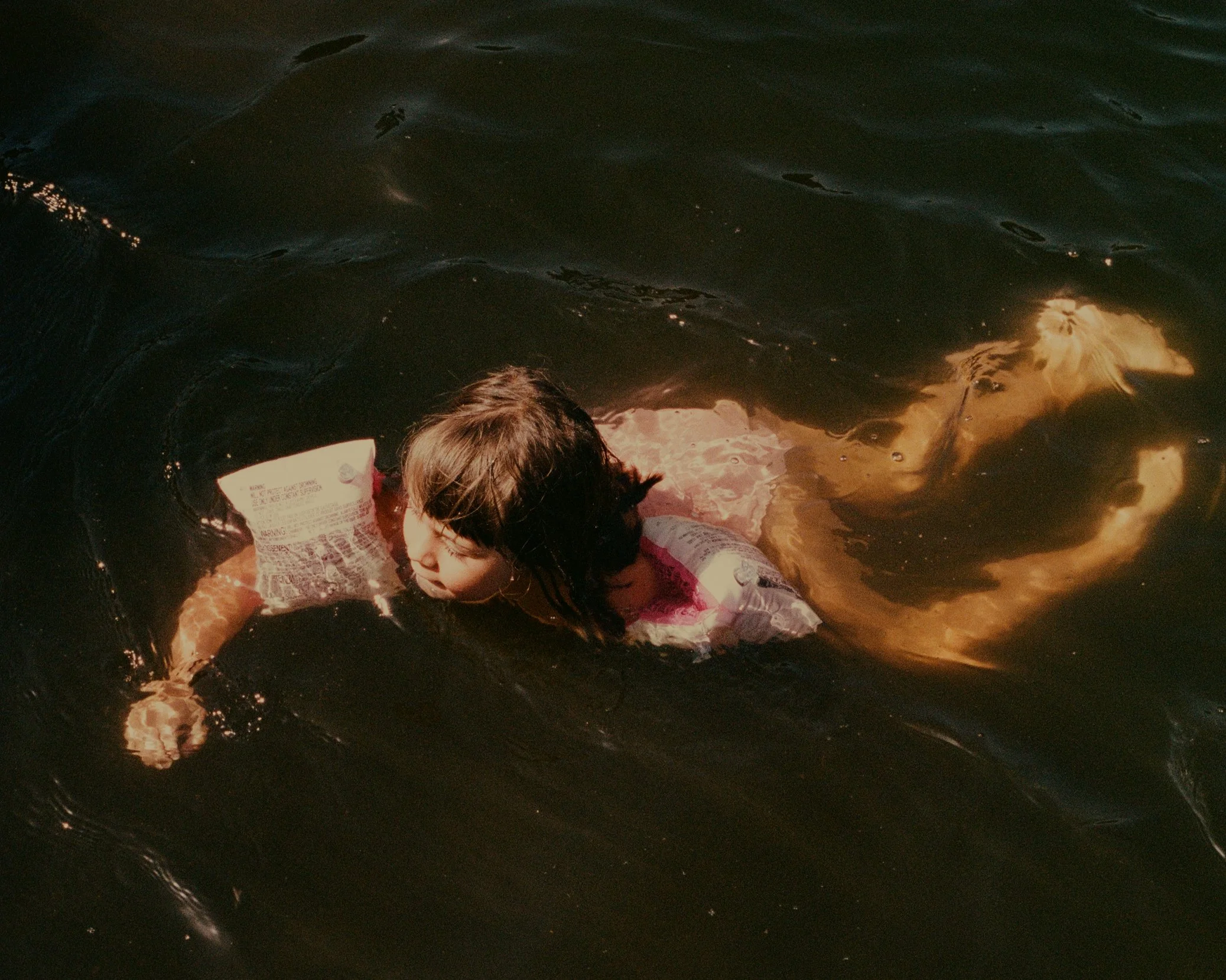 A girl swimming in dark water, wearing a life jacket.