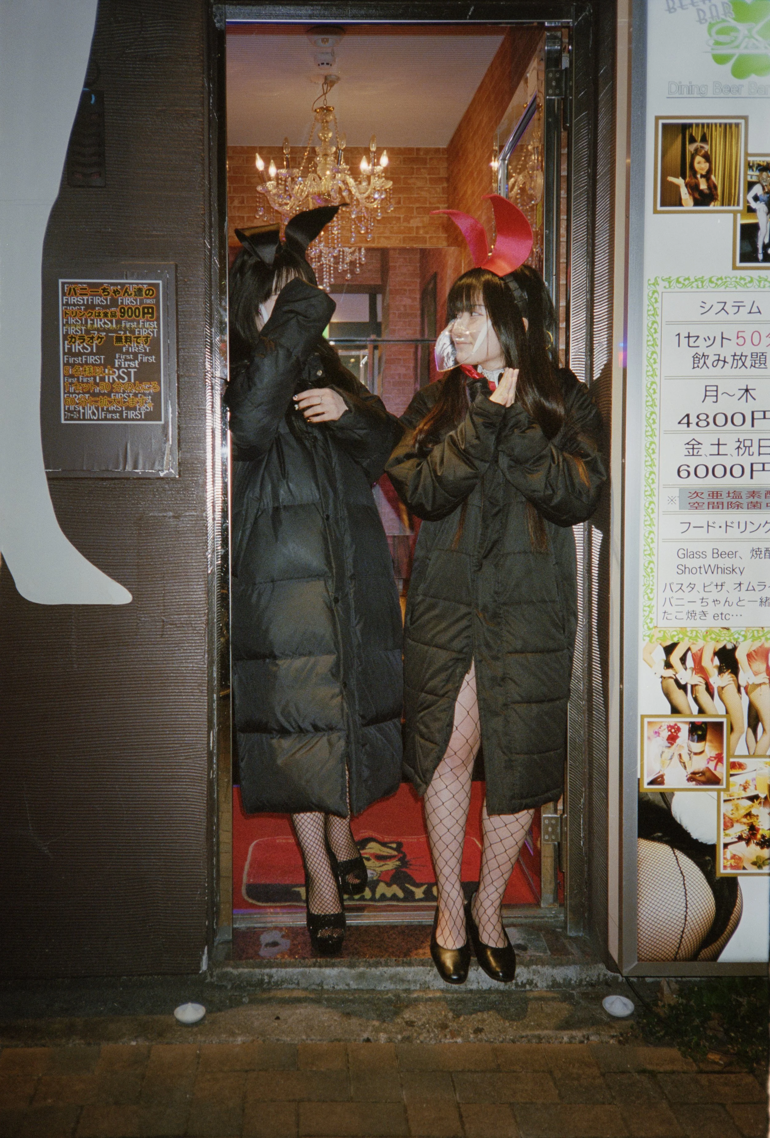 Two women wearing bunny costumes and fishnet stockings standing in a doorway of a themed restaurant or club at night.