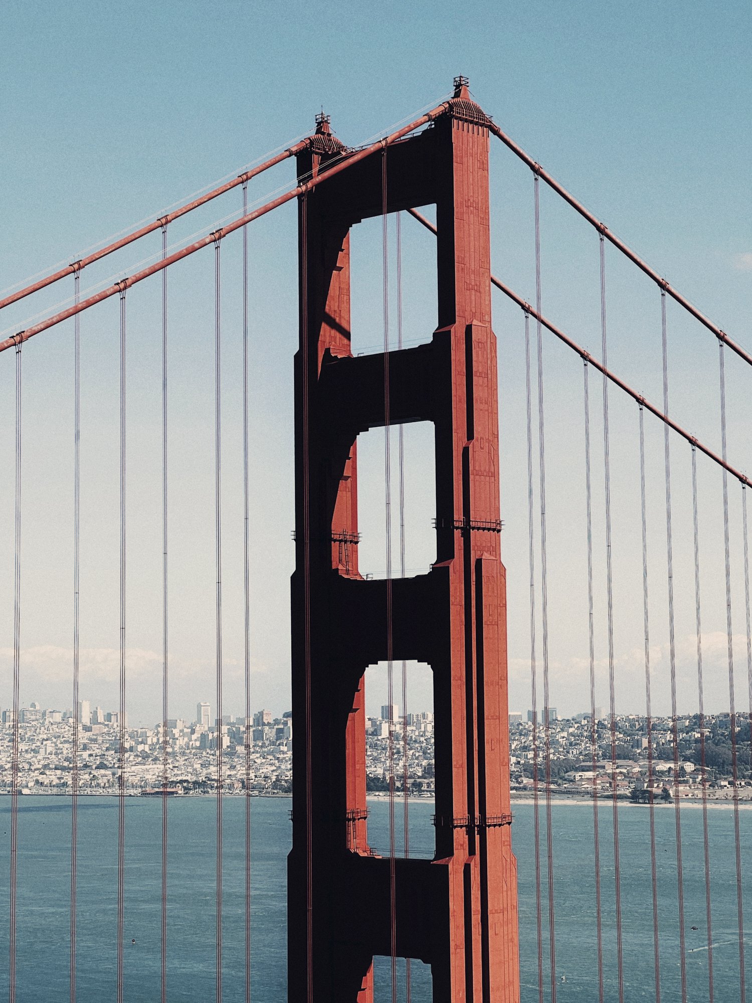 Close-up of the Golden Gate Bridge in San Francisco, with the Marin County shoreline and city in the background.
