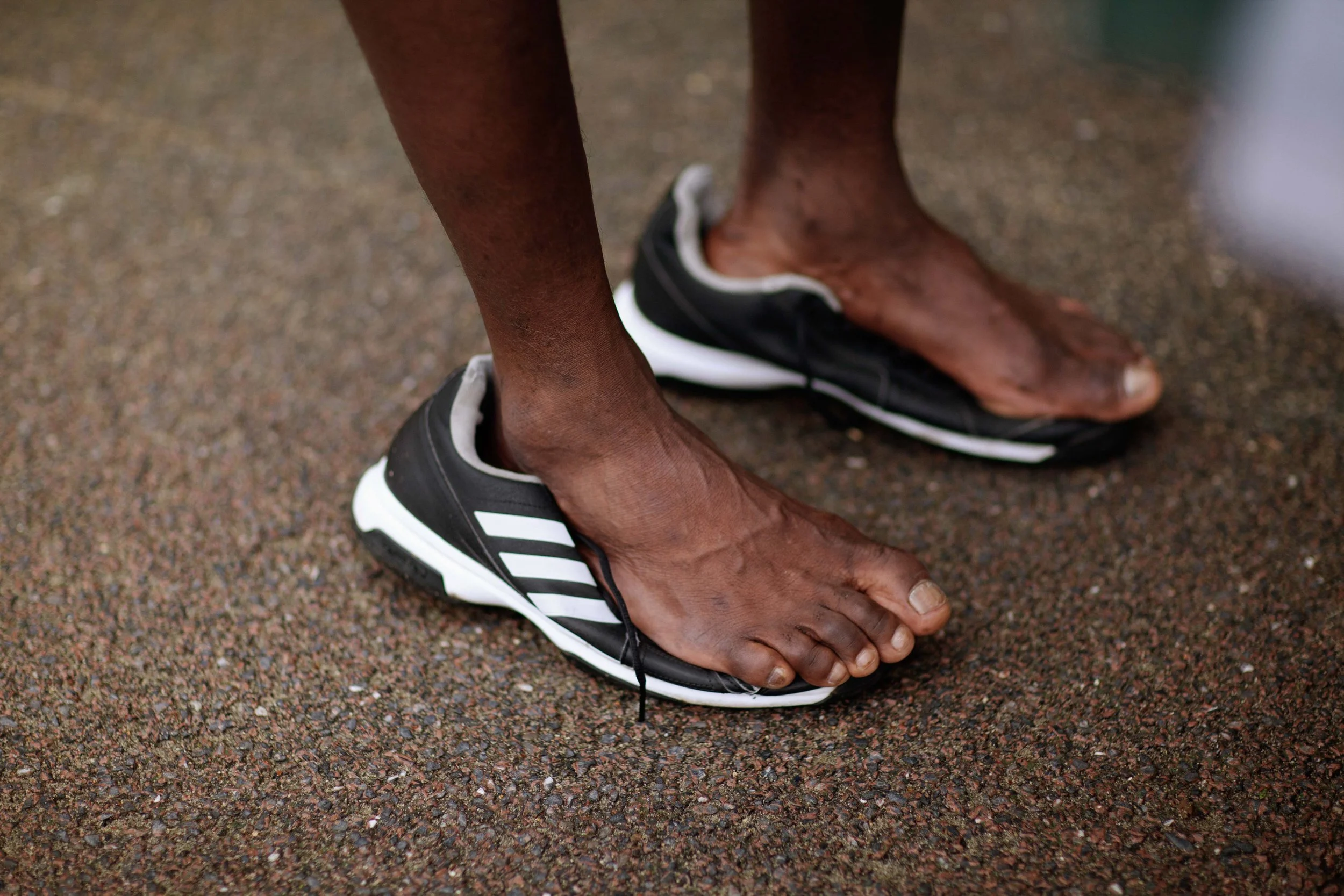 Close-up of a person's bare feet on the ground, wearing black and white athletic shoes with no socks.