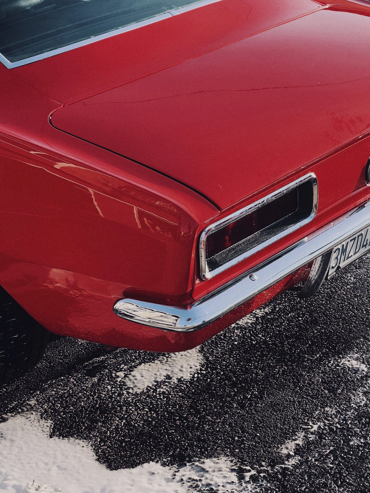 Close-up of the rear of a vintage red car with chrome details, parked on a snow-covered asphalt surface.