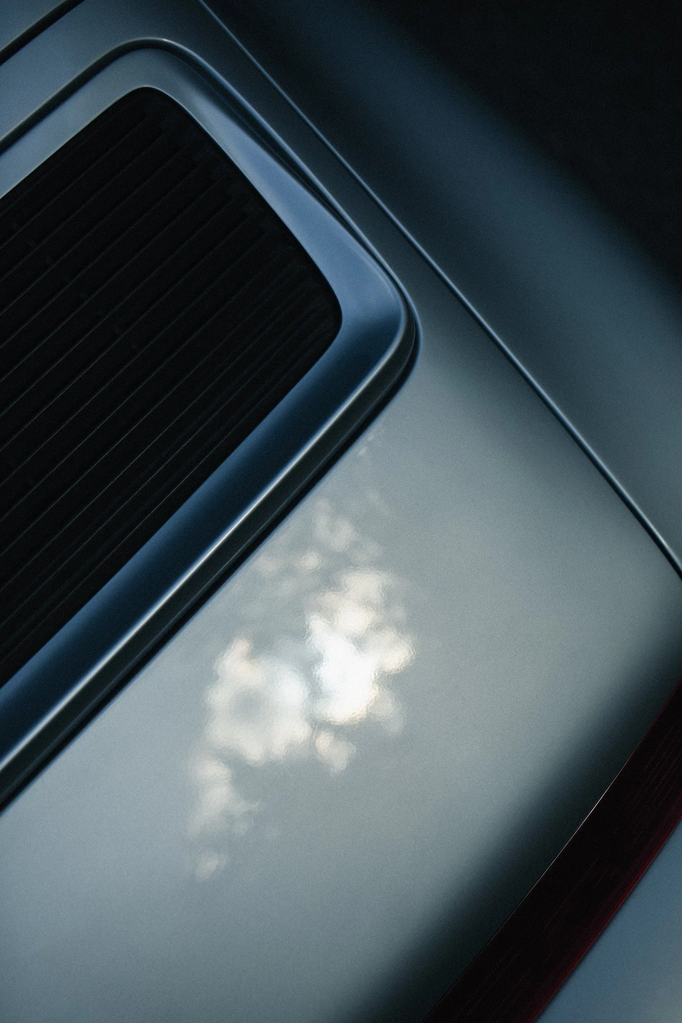 Close-up of a vintage car's hood, showing the reflection of the sky and clouds on the shiny surface.