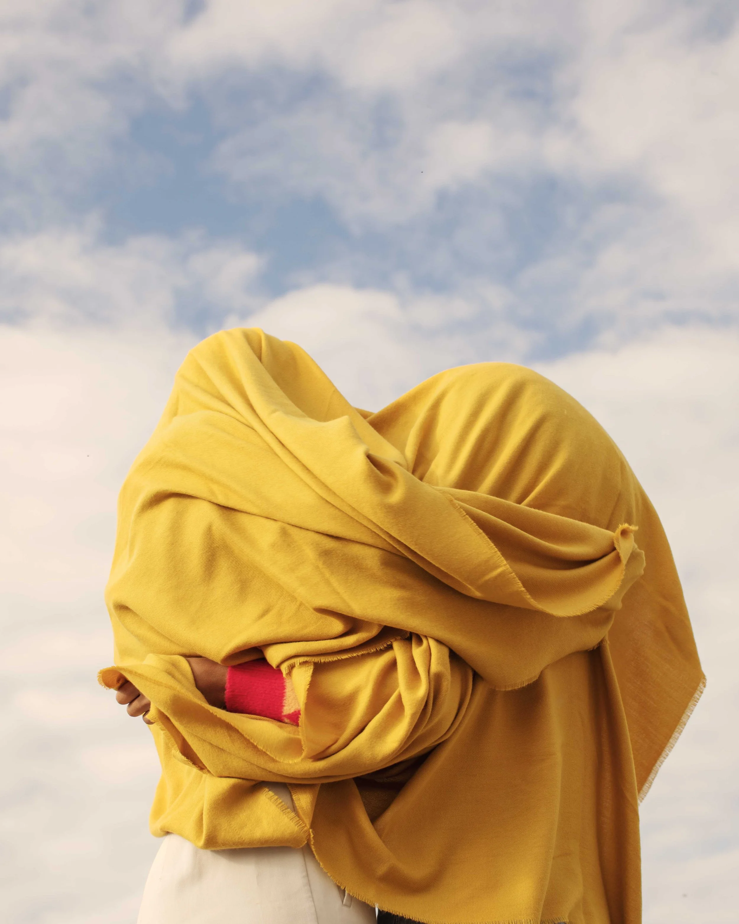 Person wearing a yellow hoodie outside against a cloudy sky.