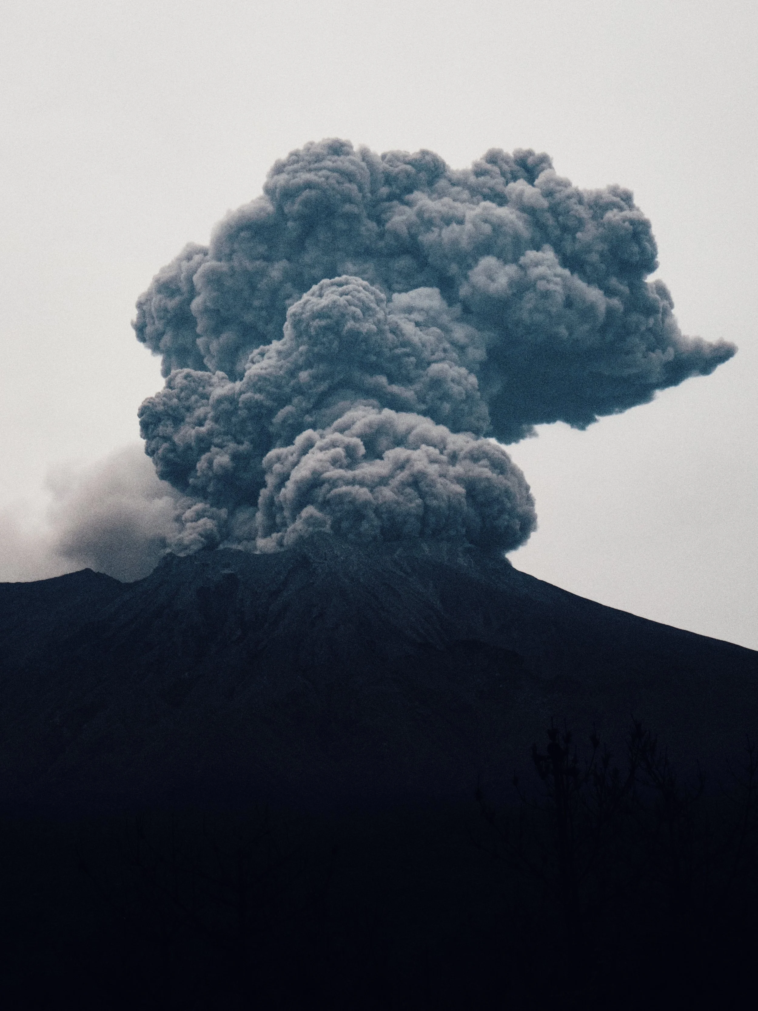 Dark volcanic mountain with a large ash plume rising into the sky.