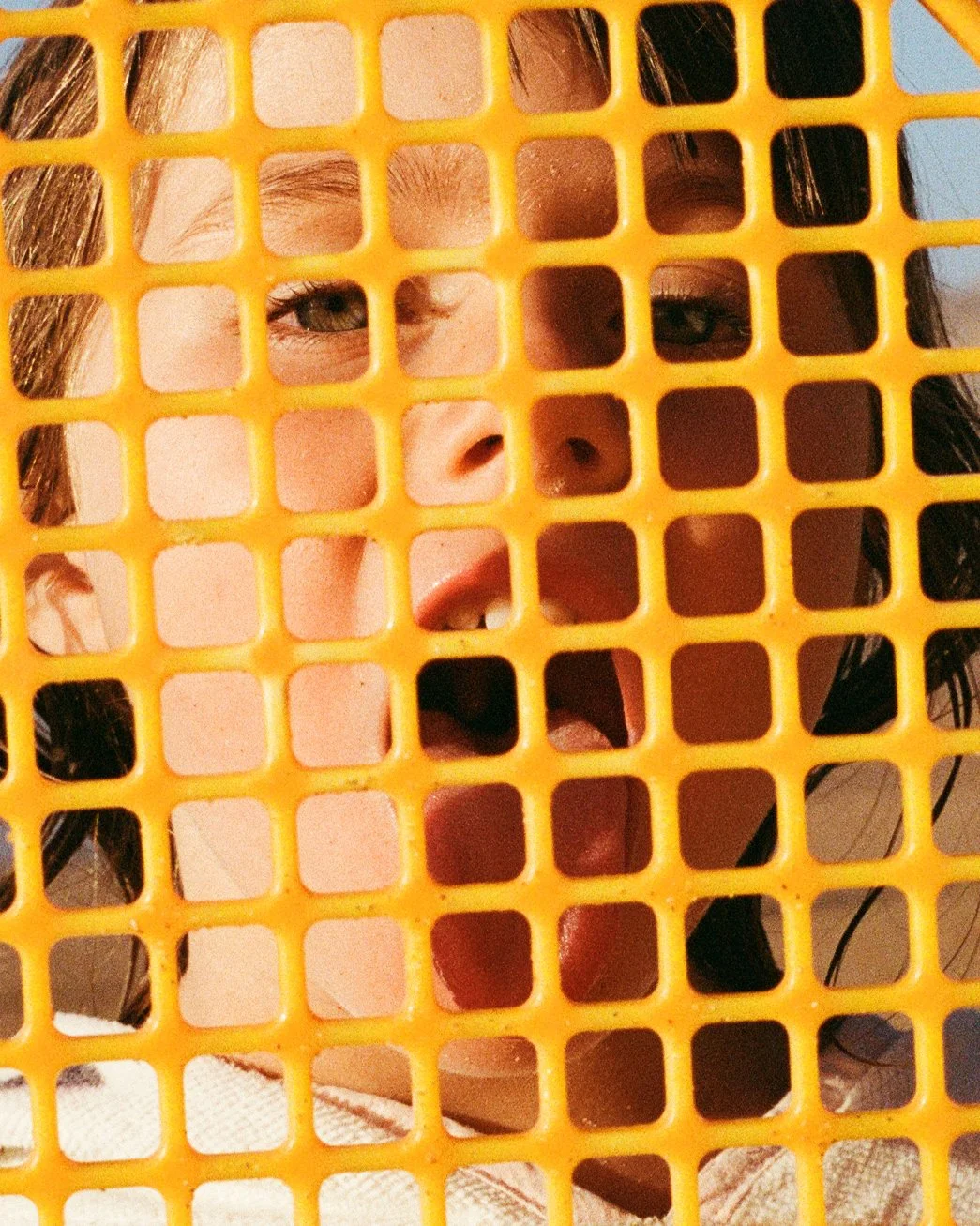 Close-up of a person's face behind a yellow plastic grid, with visible eyes and part of the nose and mouth.