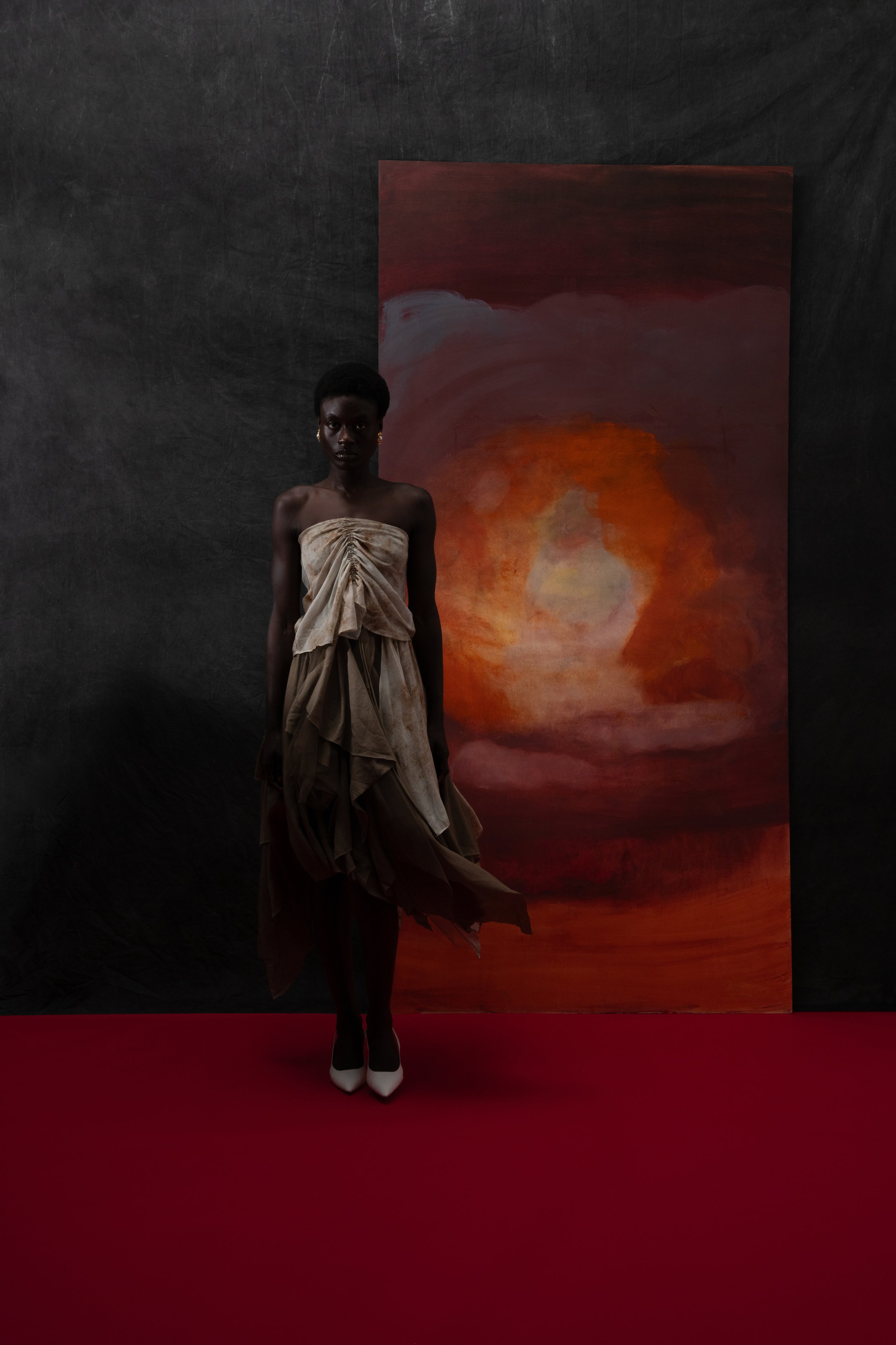 A woman standing on a red carpet in front of an abstract painting with warm colors.