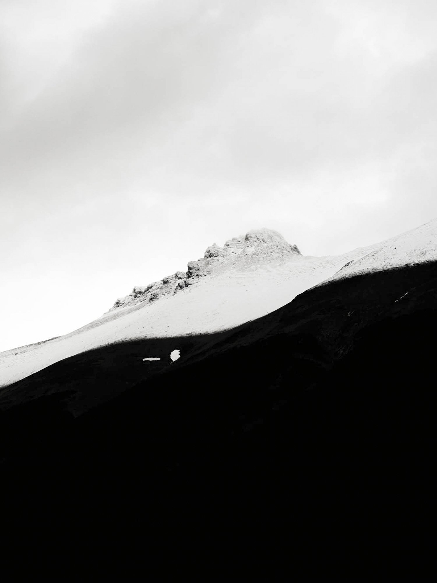Black and white photo of a mountain with a snow-capped peak and dark foreground.