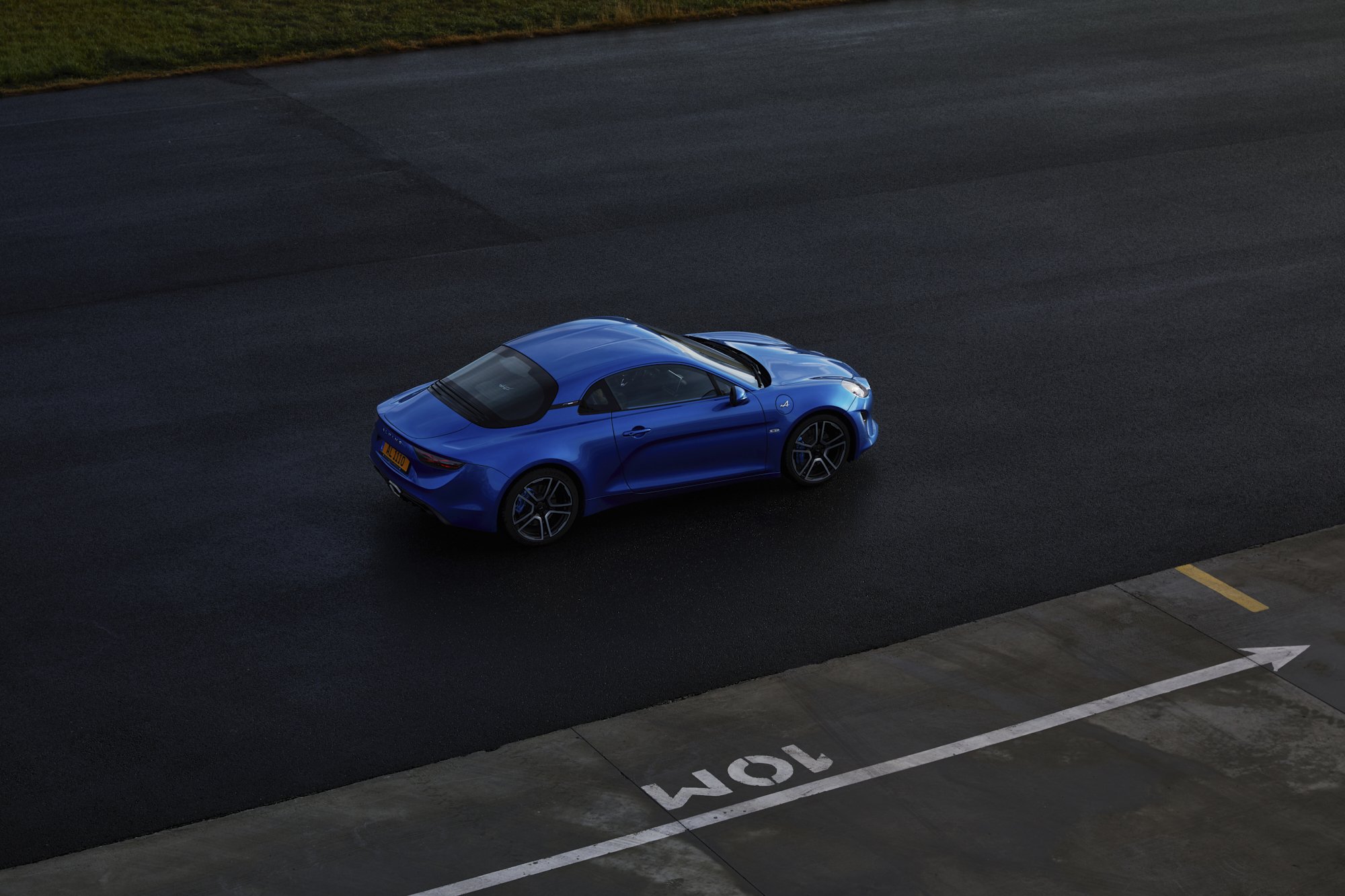 A blue sports car parked on a dark empty road near a parking space marked '10M' with an arrow, during daytime.