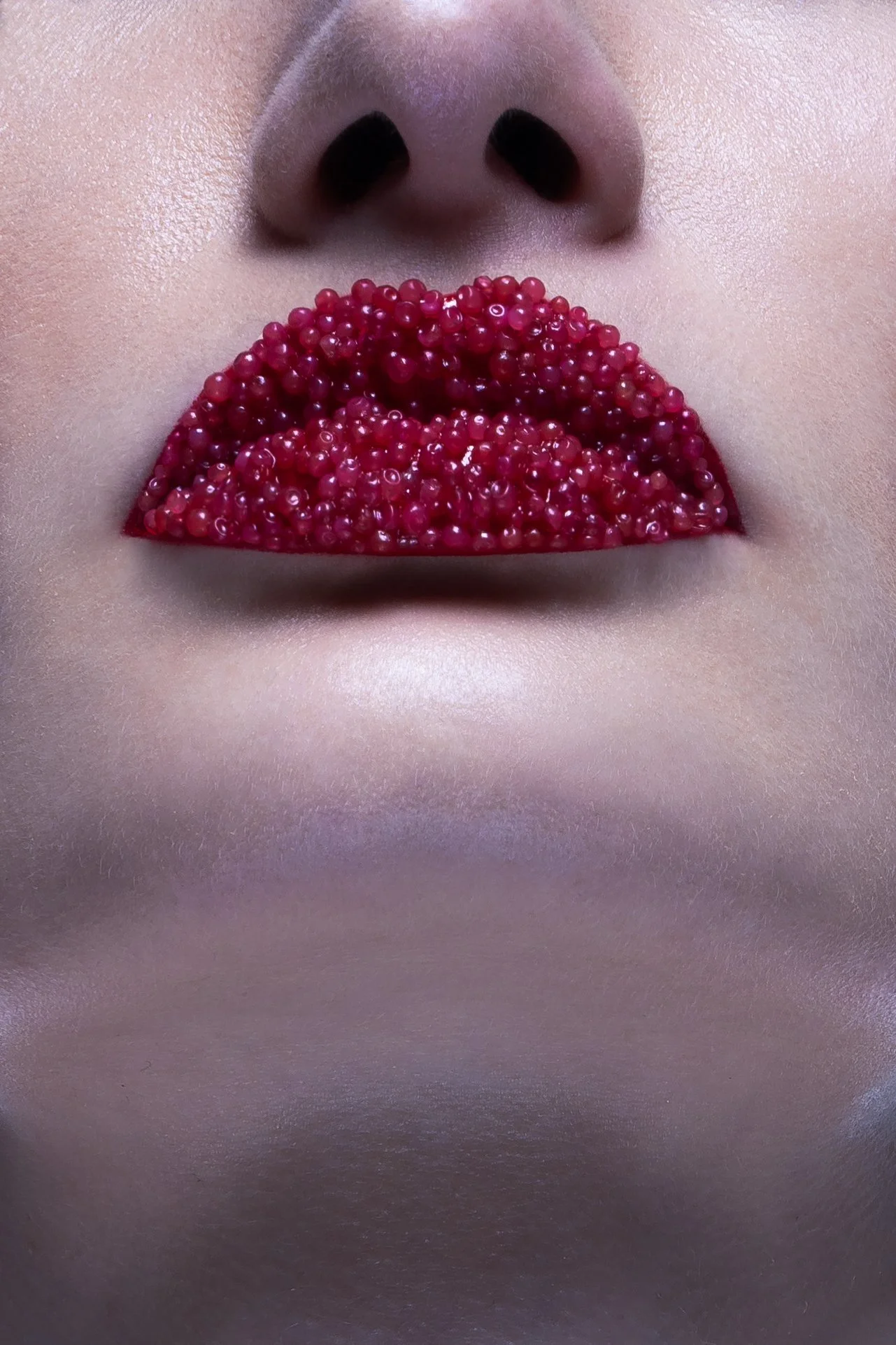 Close-up of a person's face focusing on the nose and lips. The lips are covered with small red berries, creating a unique visual effect.