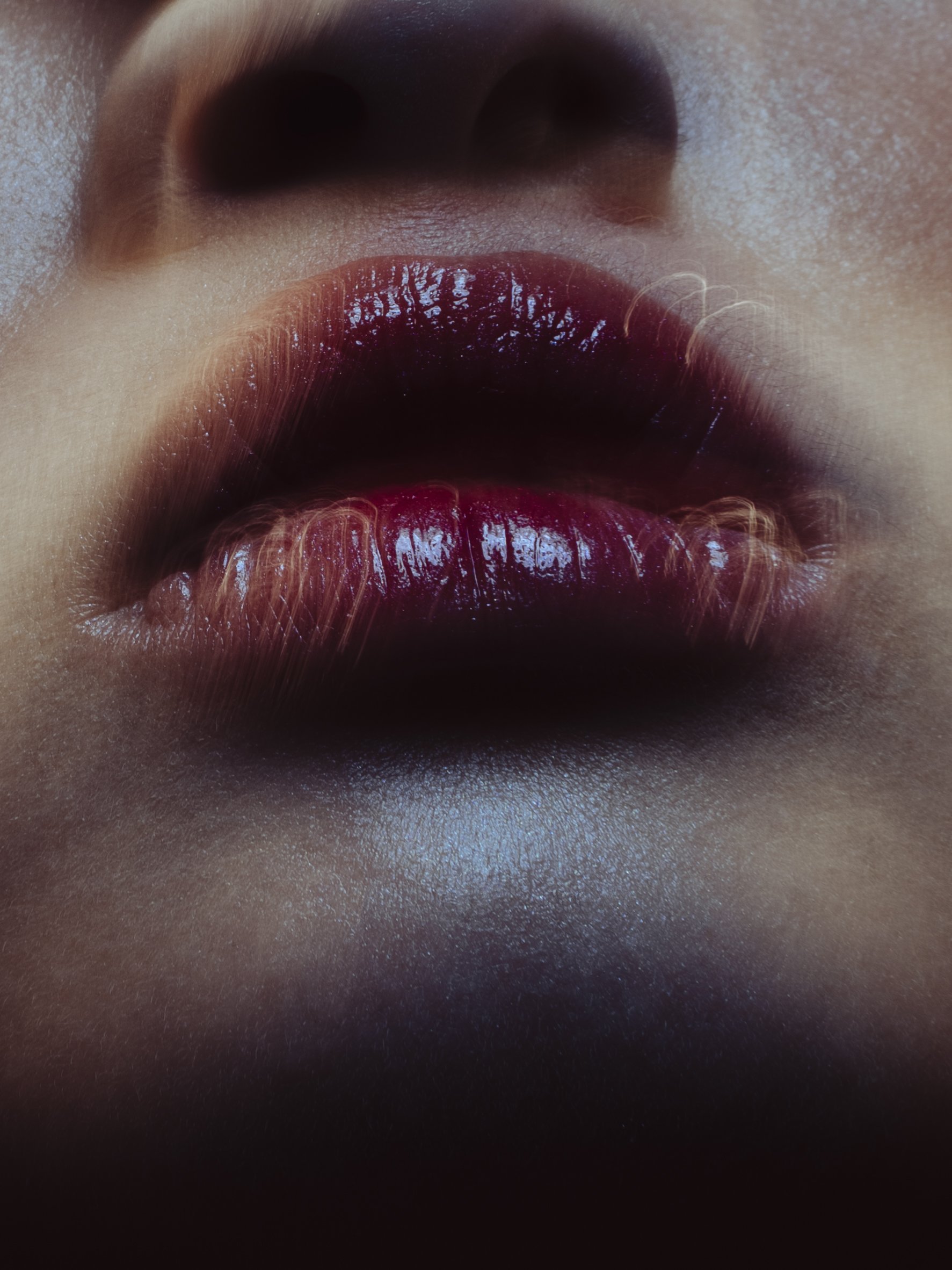 Close-up of a person's lips with shiny, dark red lipstick, viewed from below with part of the nose visible at the top.