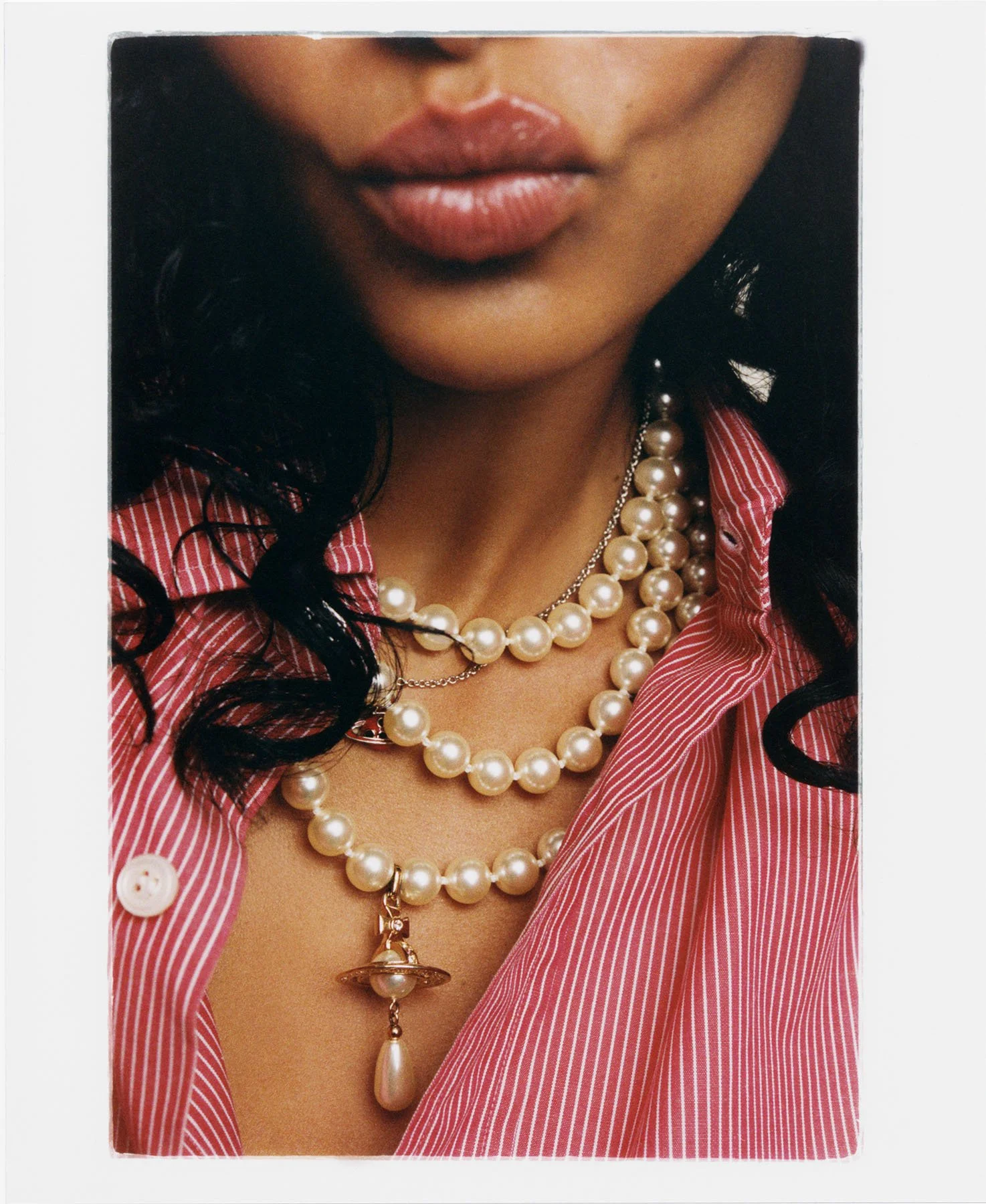 Close-up of a woman wearing layered pearl necklaces and a red and white striped button-down shirt.