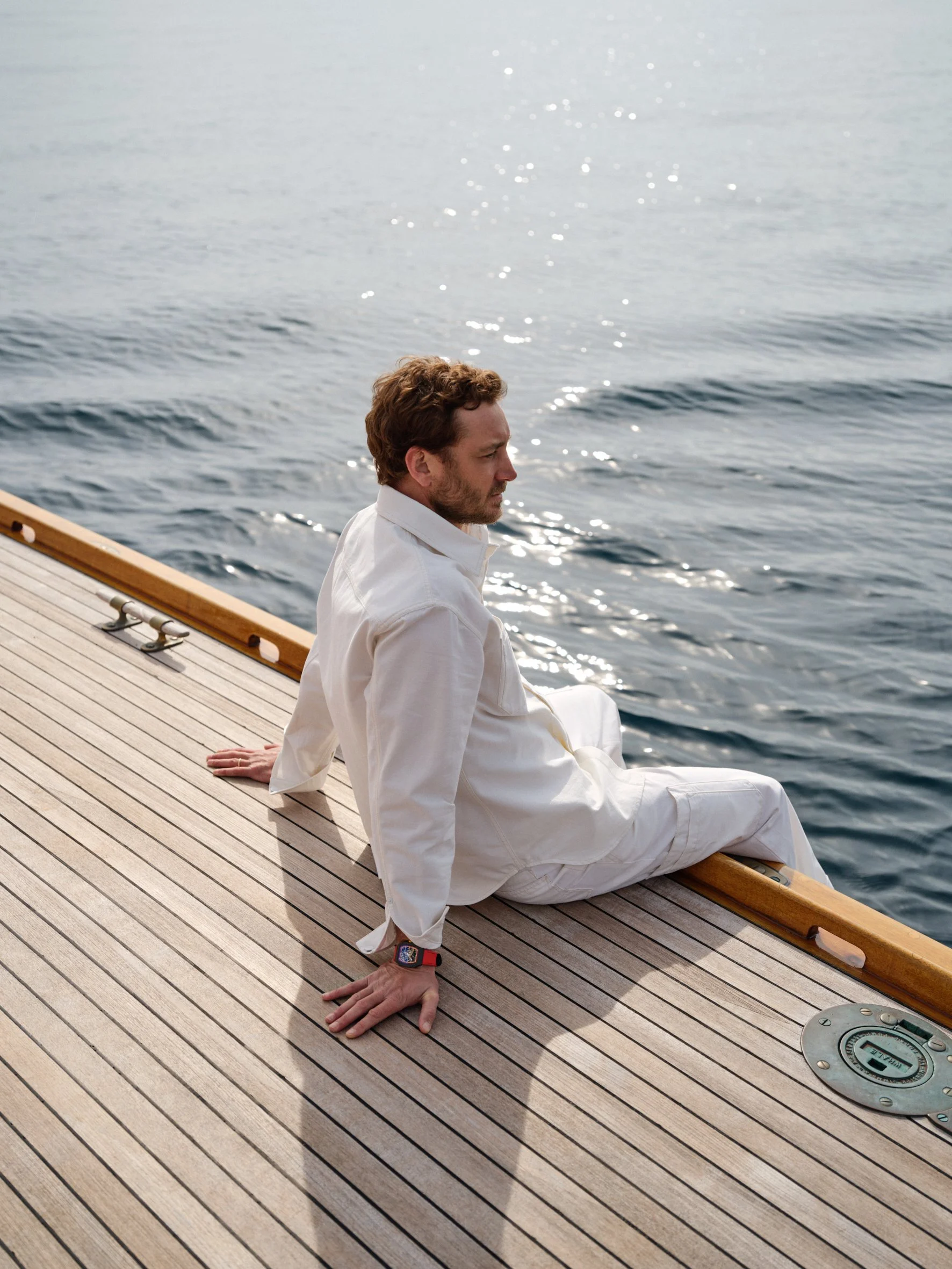 A man sitting on the deck of a boat, looking out over the water during daylight.
