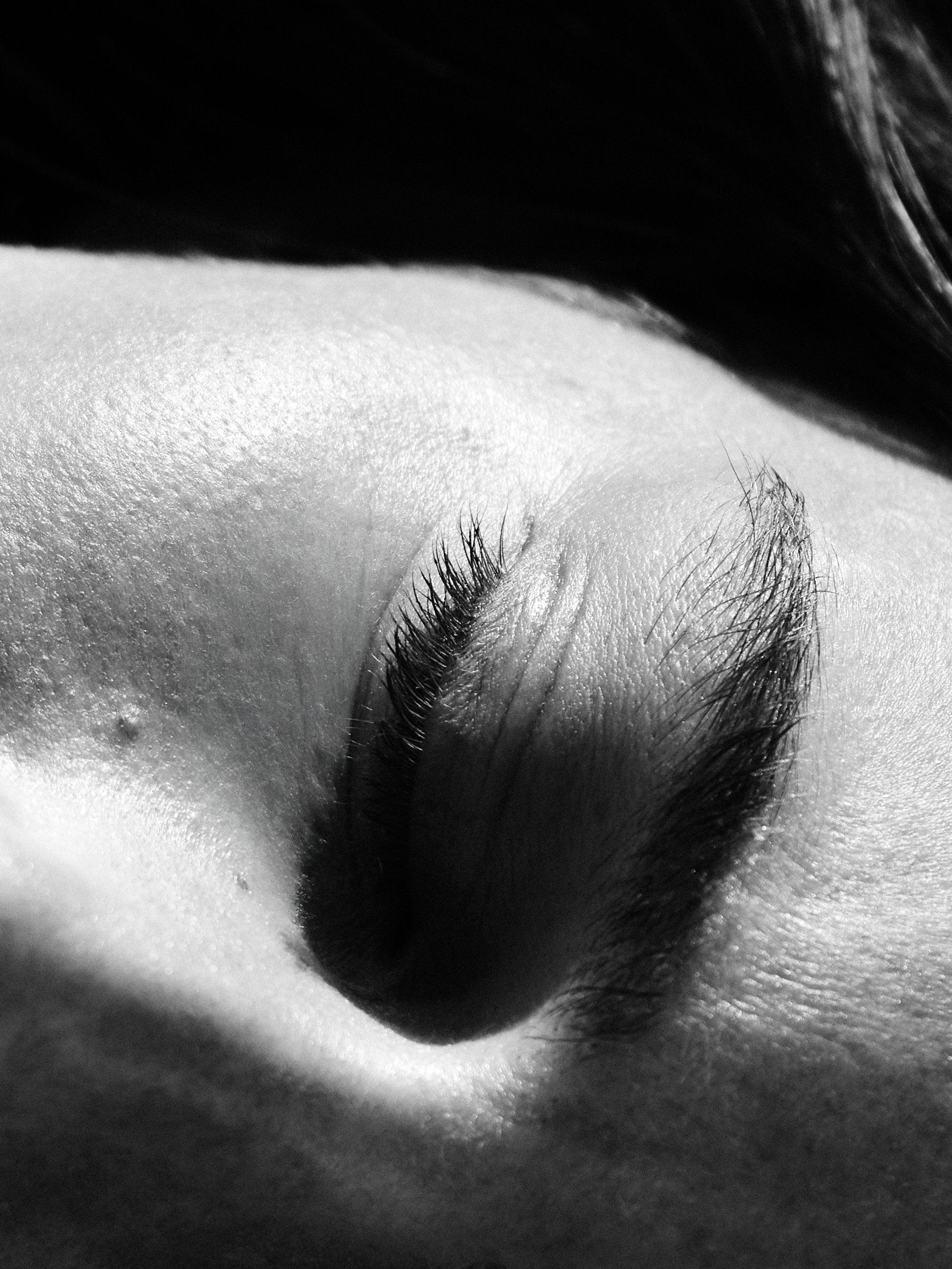 Close-up of a person's nose and closed eye, with eyelashes visible, in black and white.