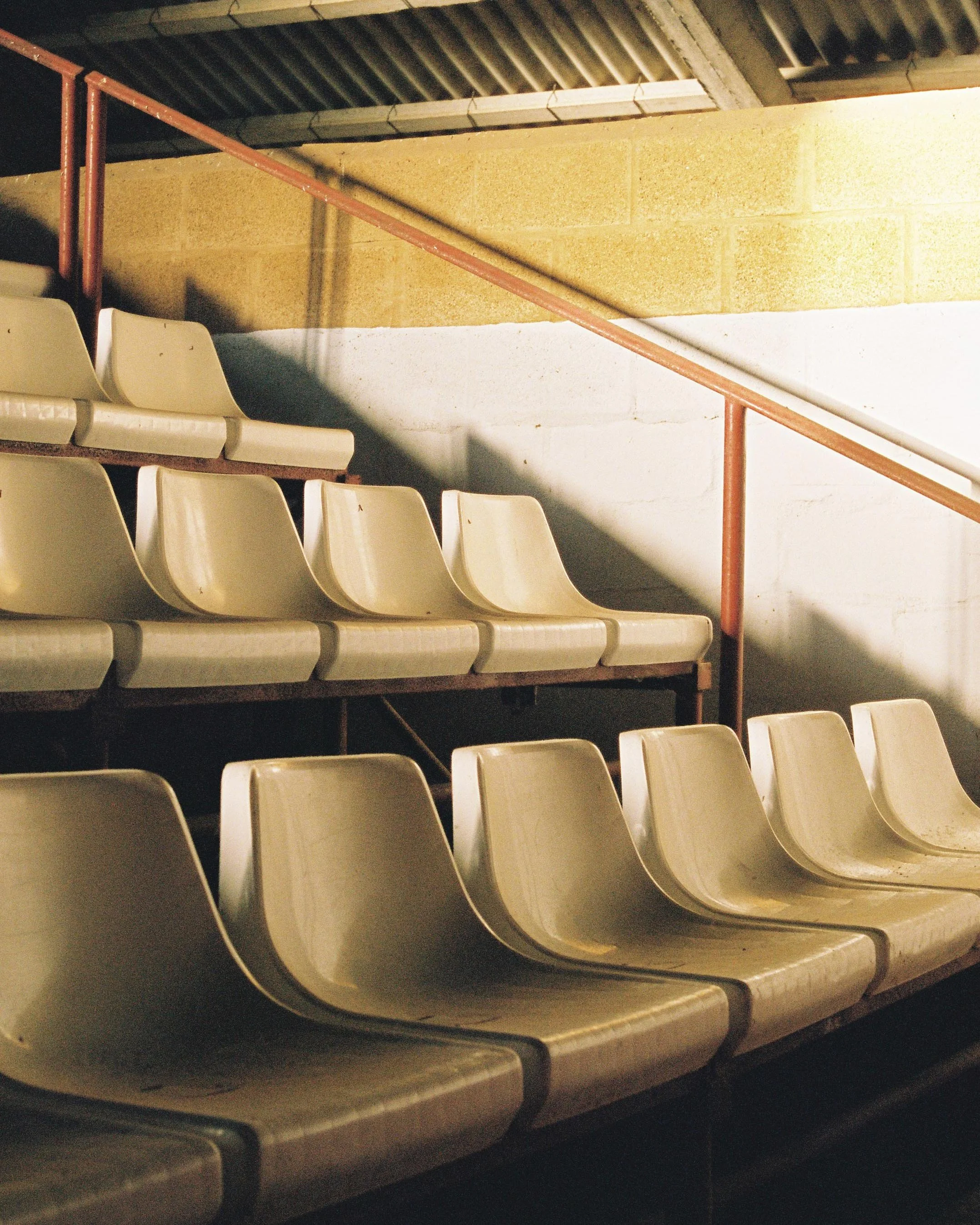 Empty beige stadium seats with a red metal railing and concrete wall in the background.